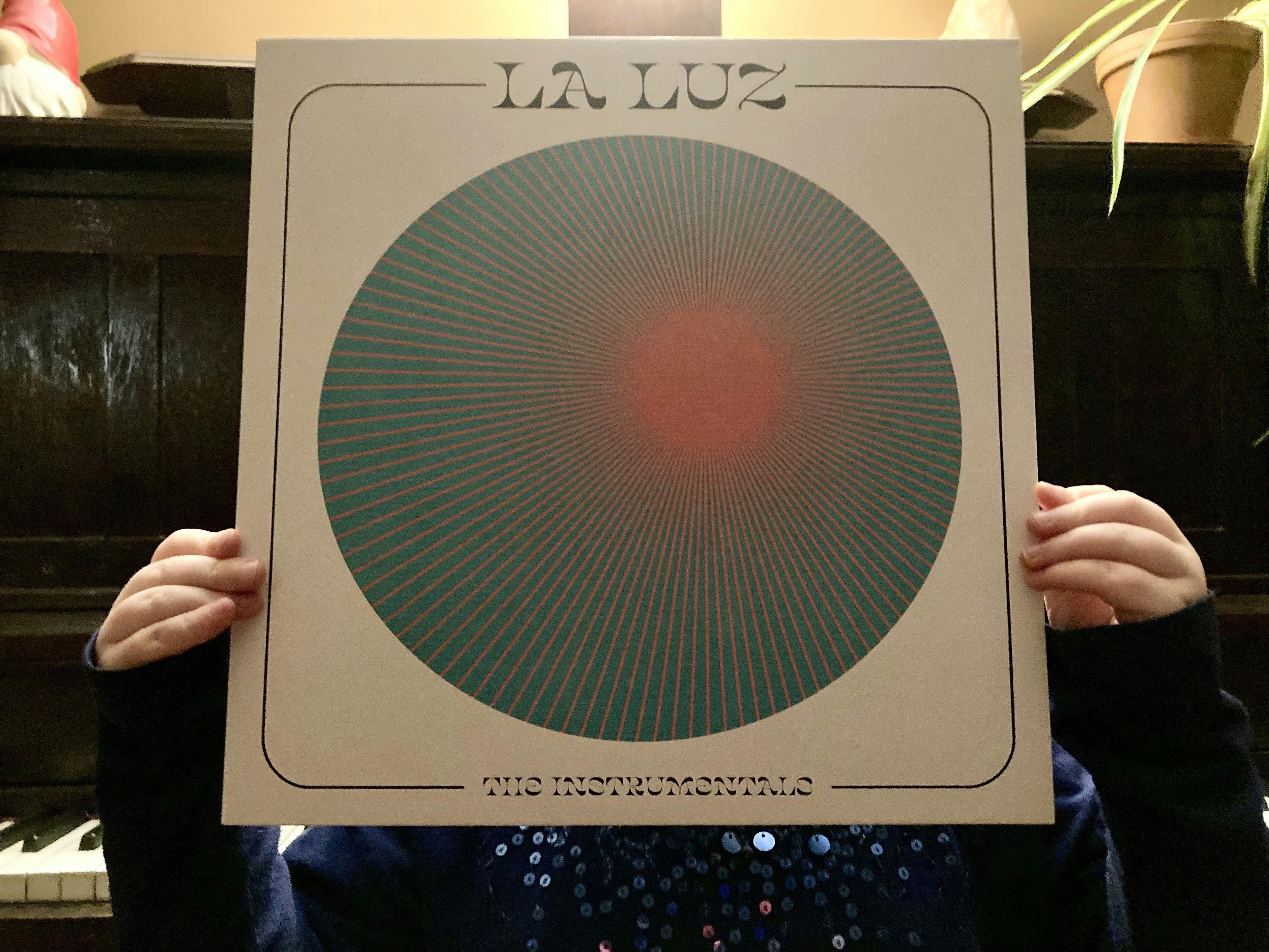 A photo of the La Luz album "The Instrumentals" being held up by a small child wearing a blue, sequinned shirt.