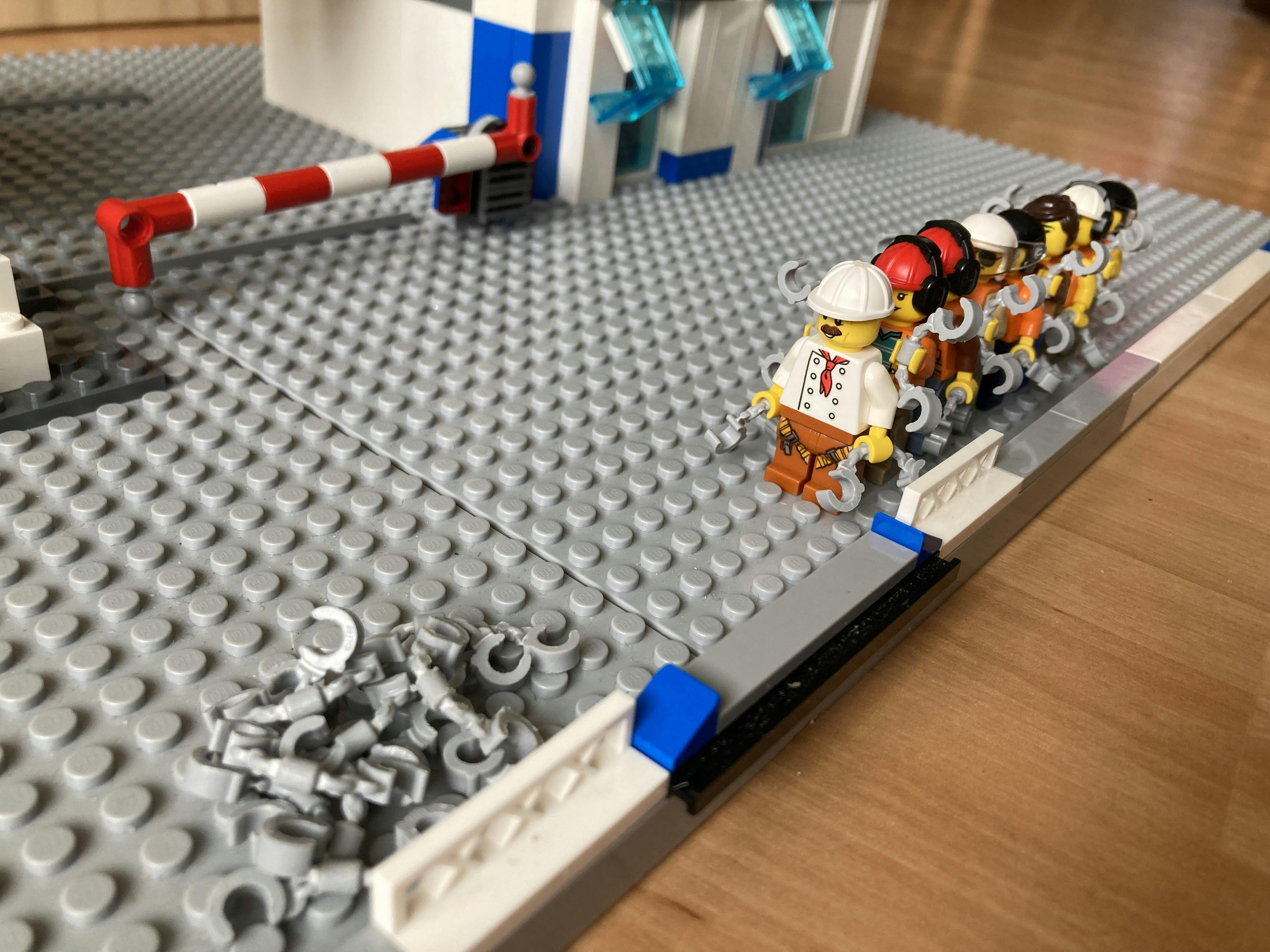 A photo of a lineup of Lego people holding handcuffs, on the way to a pile of handcuffs