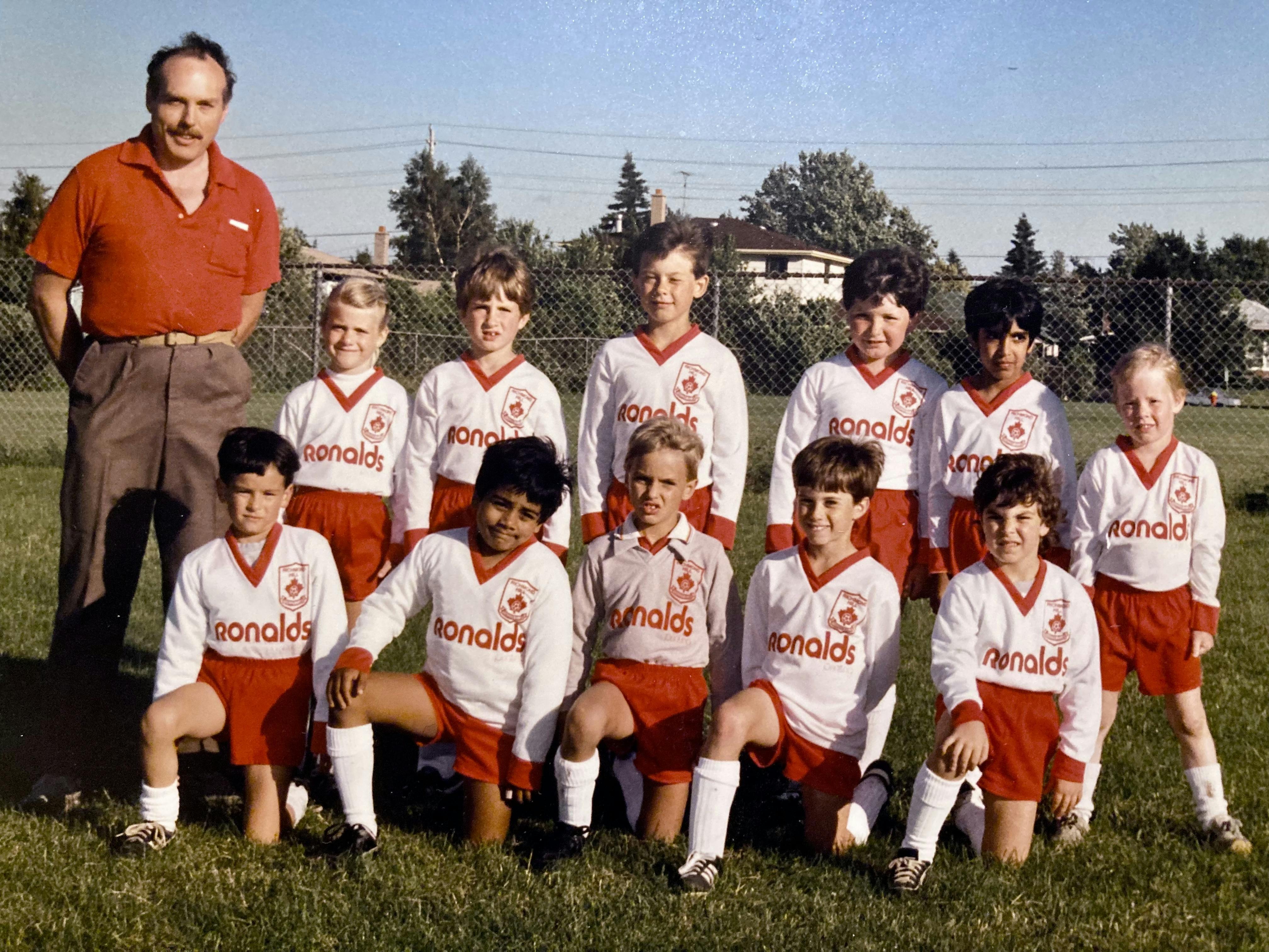 A photo of a children's soccer team in white and red uniforms and standing next to their coach who is my dad :)