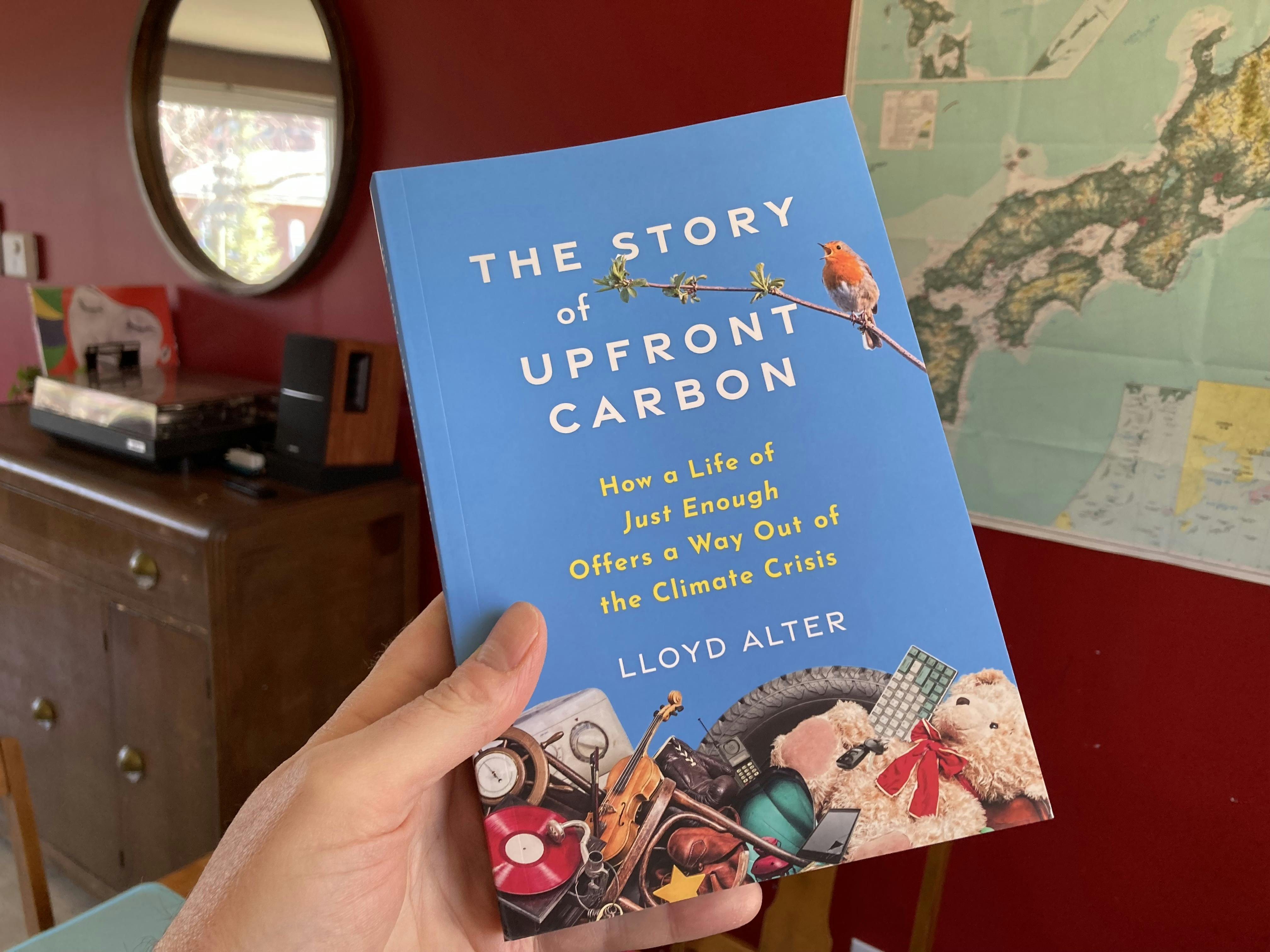A photo of Lloyd Alter's new book, The Story of Upfront Carbon, being held by my hand, with a record player and a map of Japan in the background.