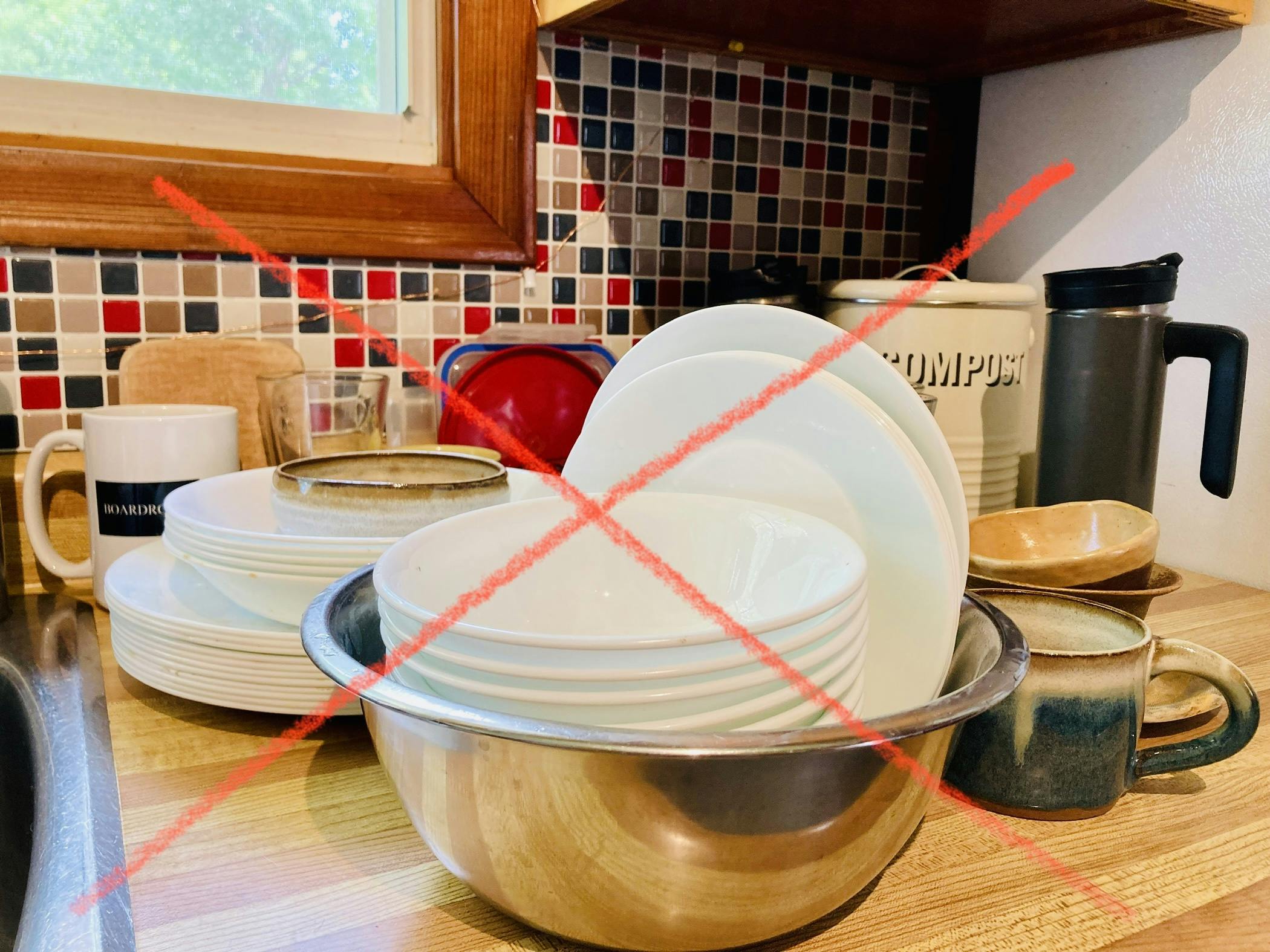 A photo of a pile of dirty dishes by the sink with a big red X over them.