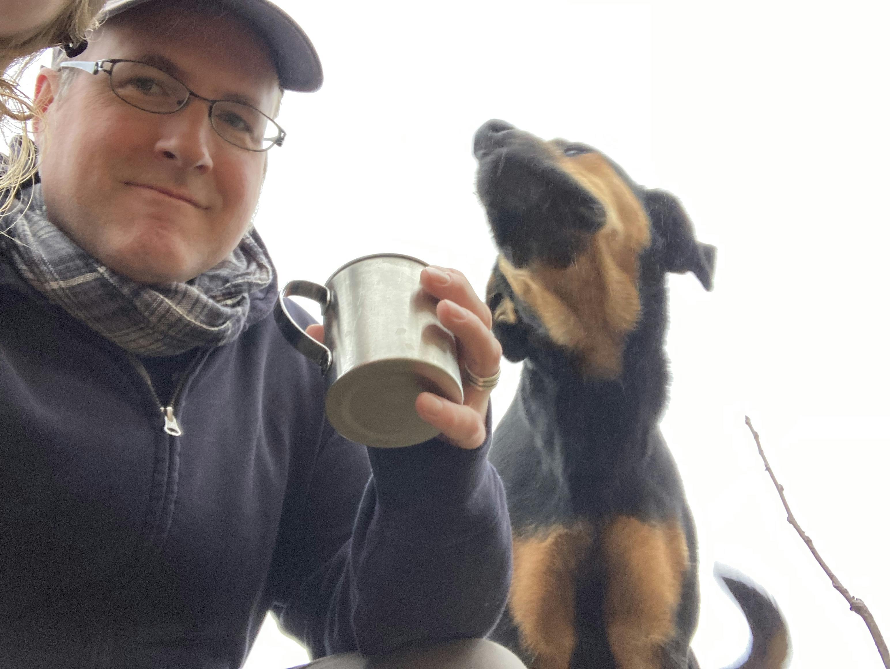 A photo of a man, holding a metal mug, and a dog, from below.