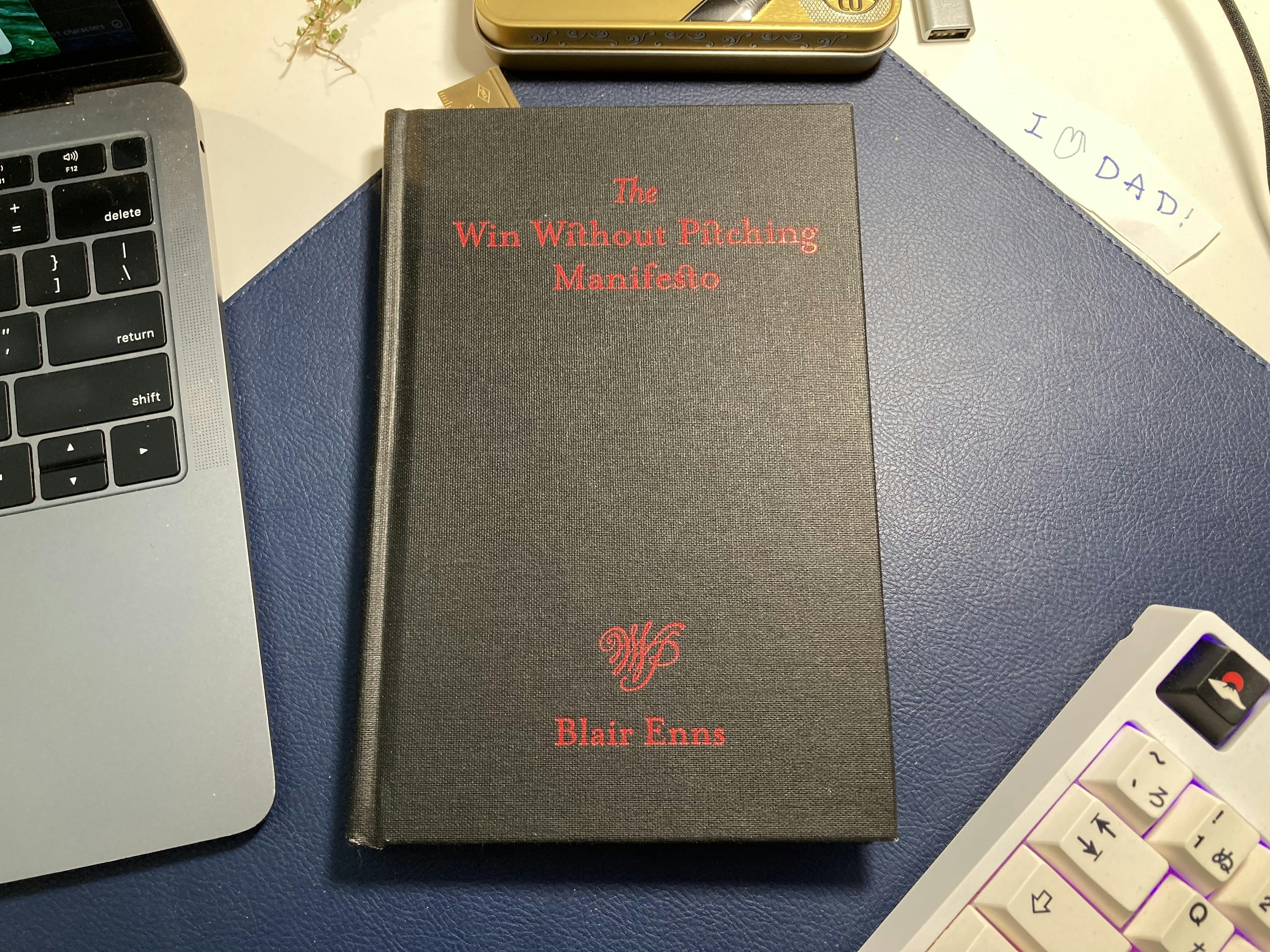 A picture of Blair Enns' book "The Win Without Pitching Manifesto," in black cloth binding with the title printed on in a red foil finish