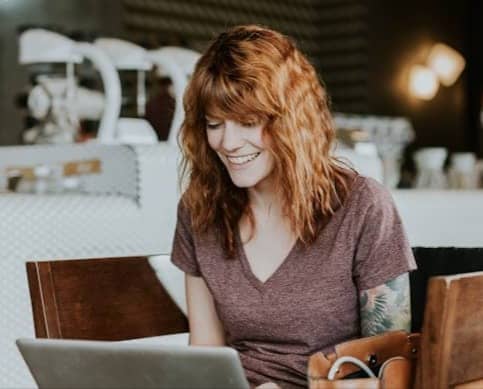 woman sitting on brown wooden chair while using silver laptop computer in room