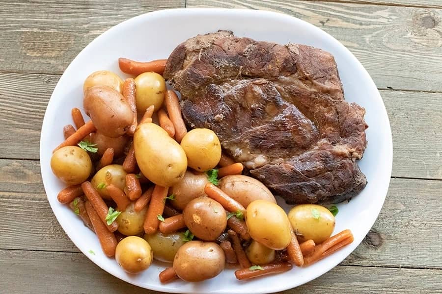 Slow cooker roast beef dinner with potatoes, carrots and a chuck roast on a white platter.