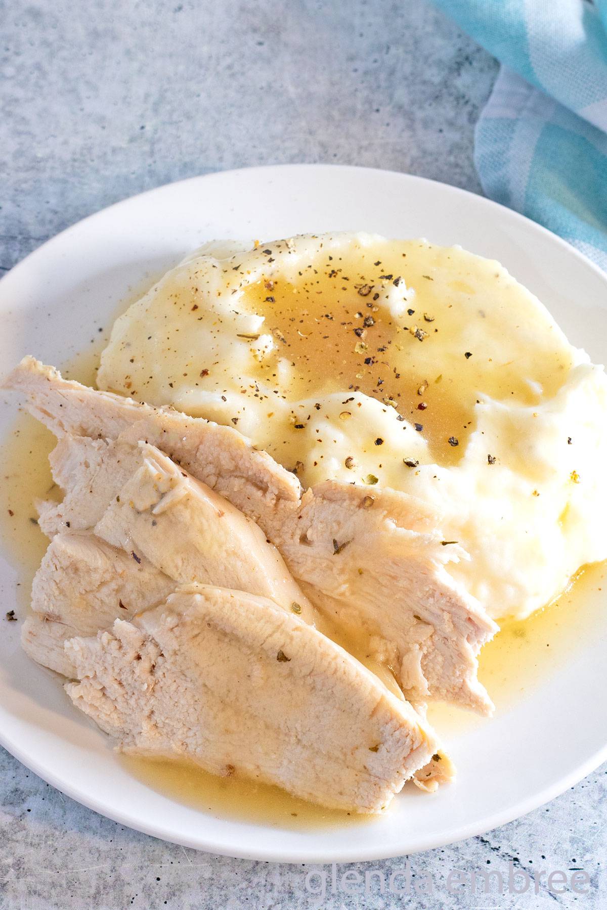 Convection Oven Turkey in a Bag sliced and served on a white plate with mashed potatoes and gravy.
