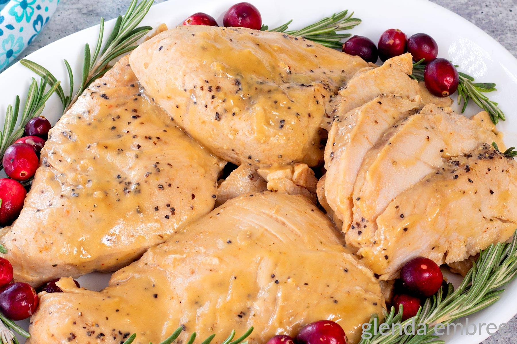 Crockpot Turkey Tenderloins drizzled with gravy on a white platter with cranberries and rosemary sprigs for garnish.