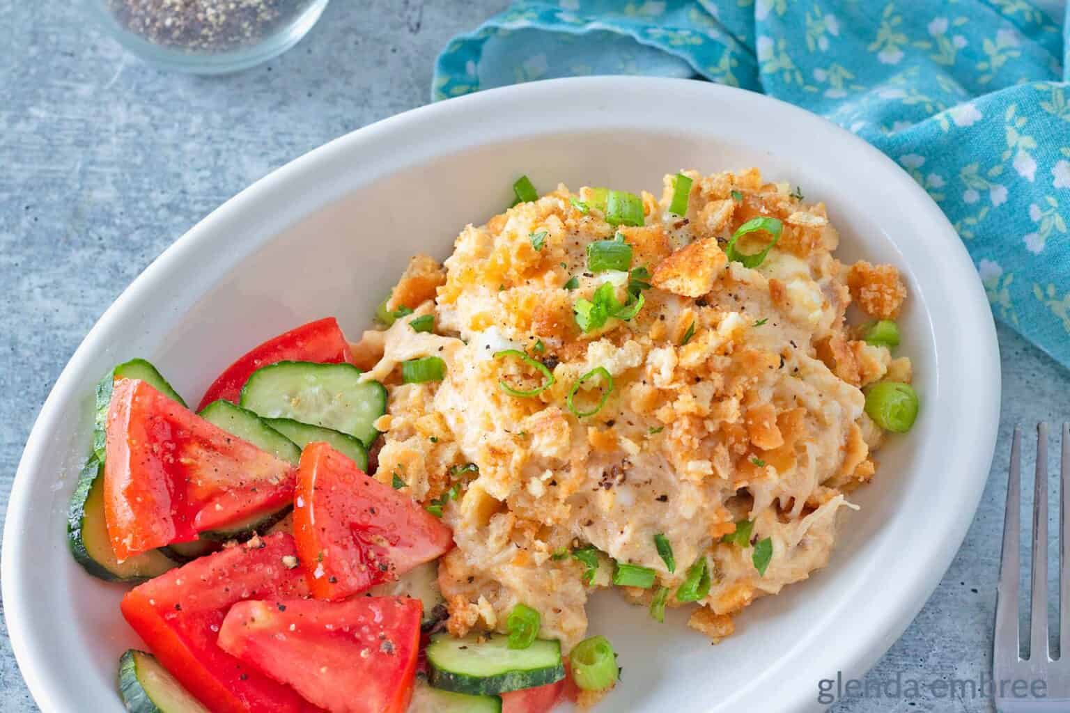 Million Dollar Chicken Casserole served with cucumber and tomato salad in a white low-sided dish.