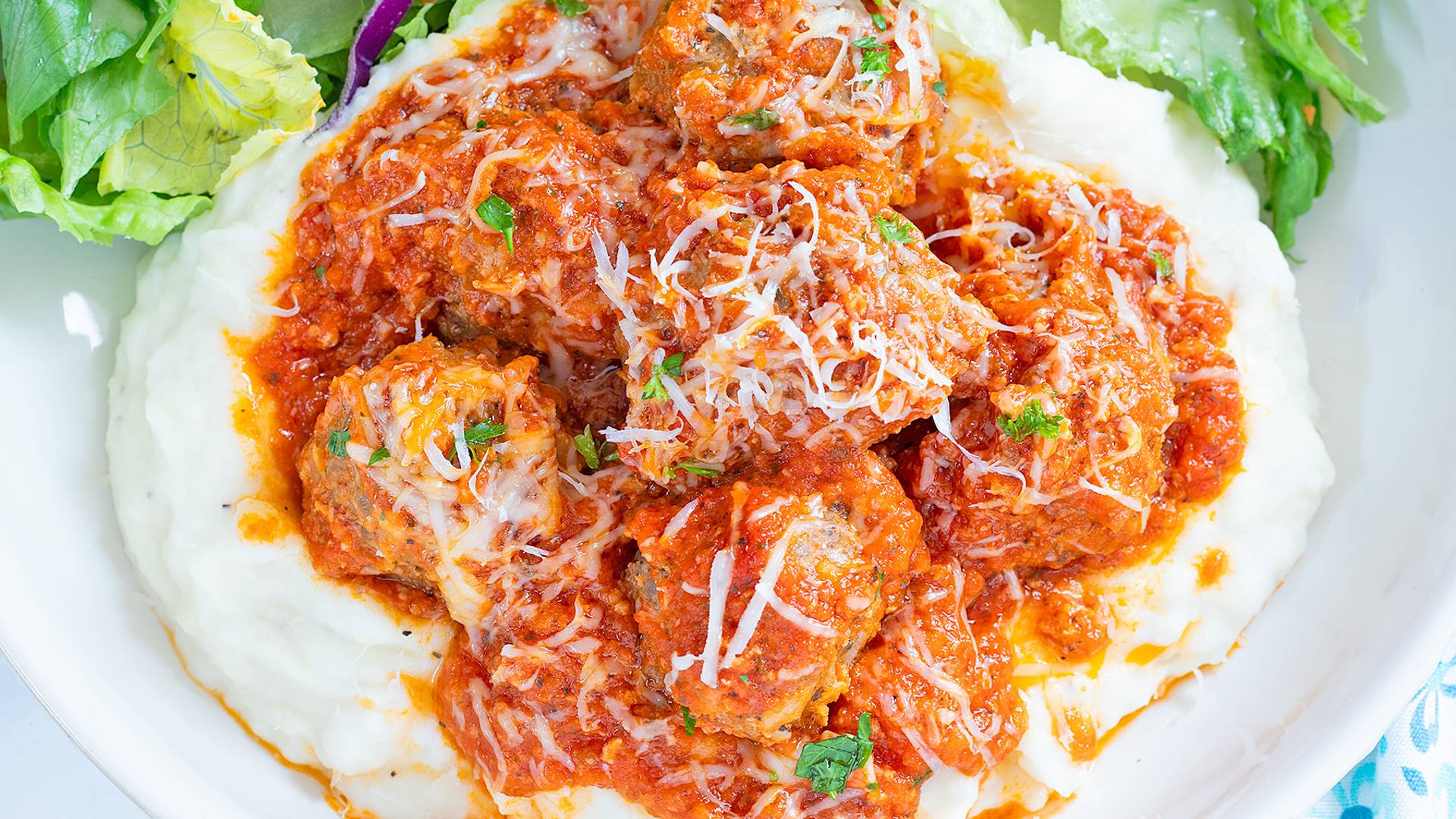 Porcupine Meatballs over mashed potatoes on a white plate with salad.