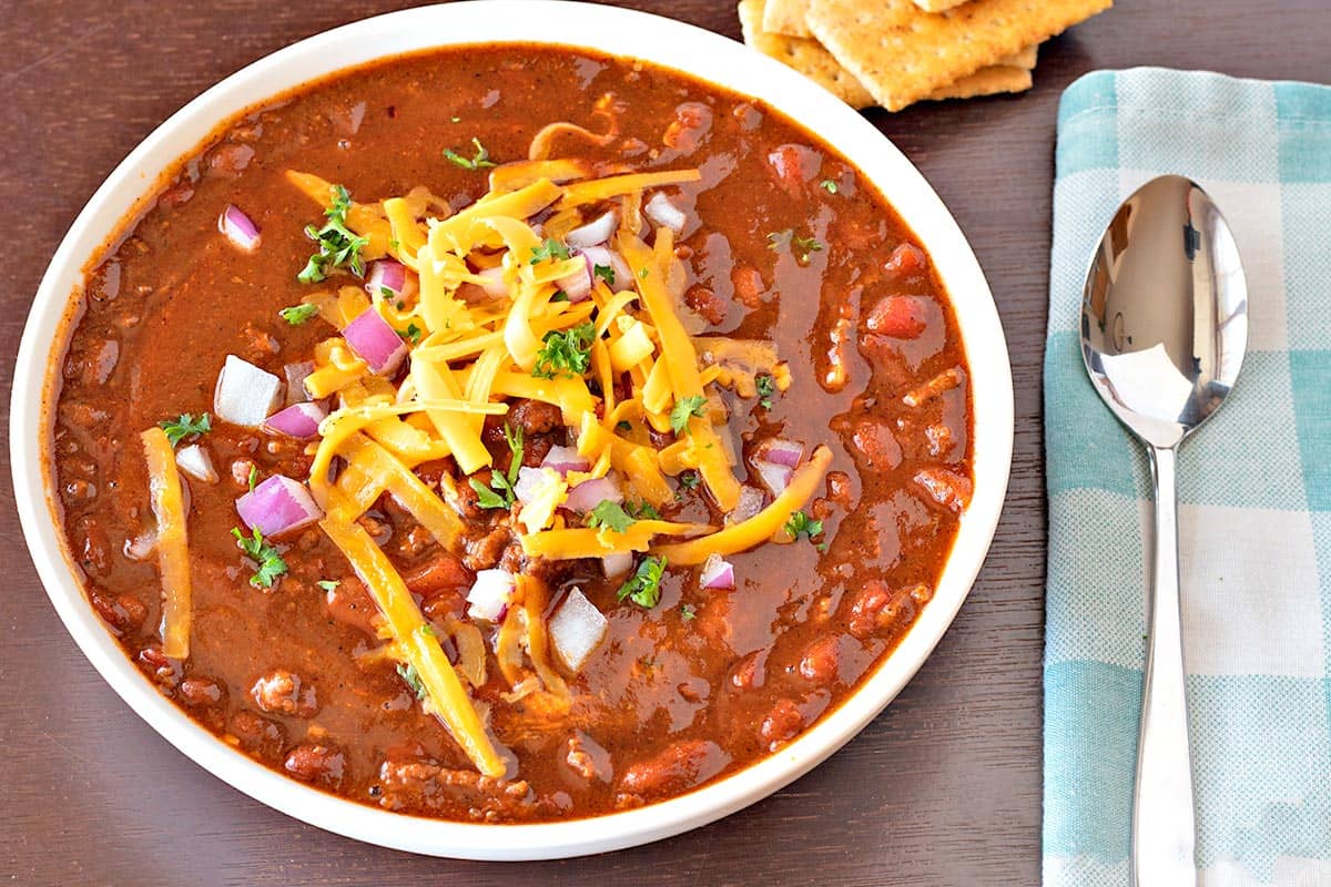 Easy chili in a white ceramic bowl topped with grated cheddar, minced red onion and parsley.