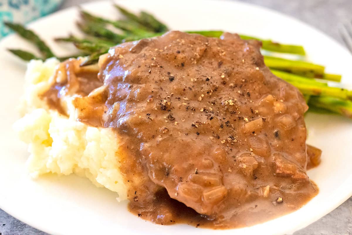 Slow Cooker Beef Cube Steak and mashed potatoes on a white plate with roasted asparagus.