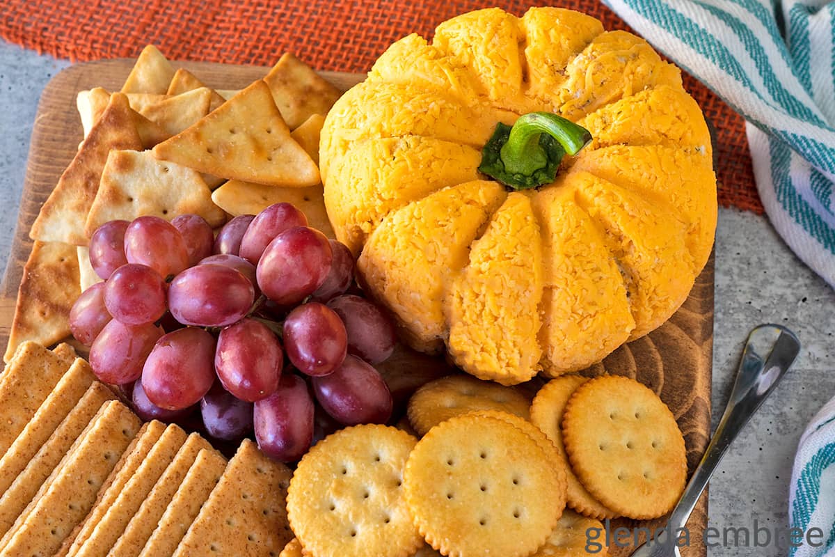 Cheese Ball in the shape of a pumpkin on a board with red grapes and assorted crackers.