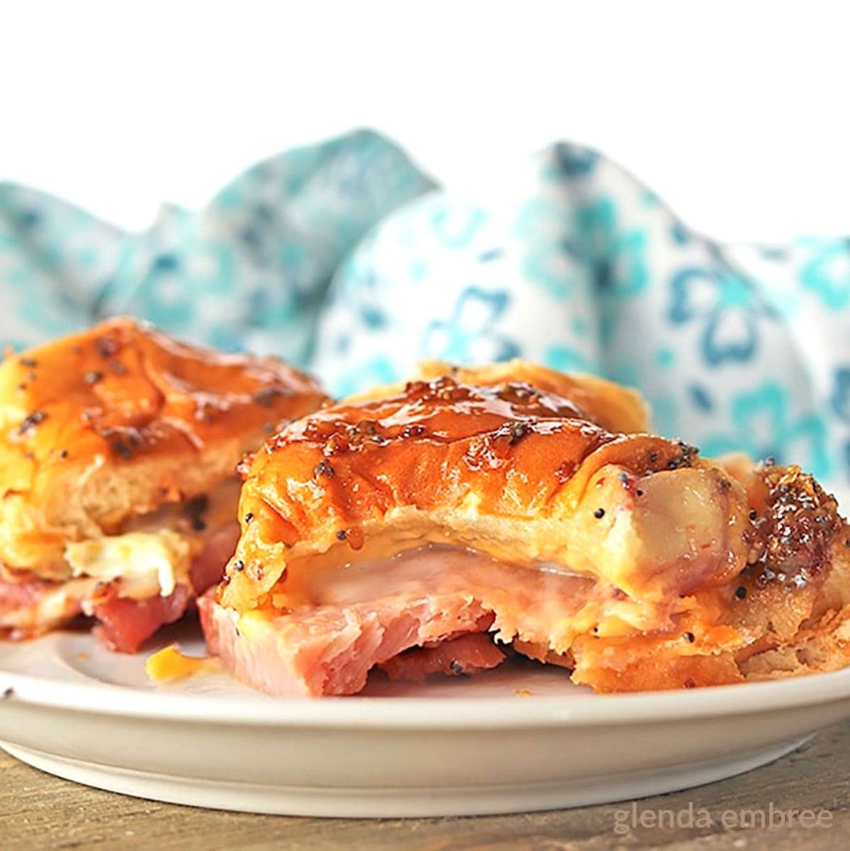 Two baked Ham and Cheese Sliders on a white plate.