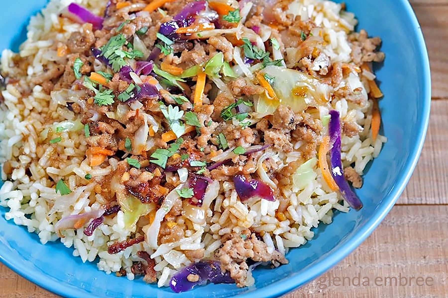 Egg Roll Bowl with Quick and Easy Ground Pork Egg Roll filling over Brown rice in a blue ceramic bowl.
