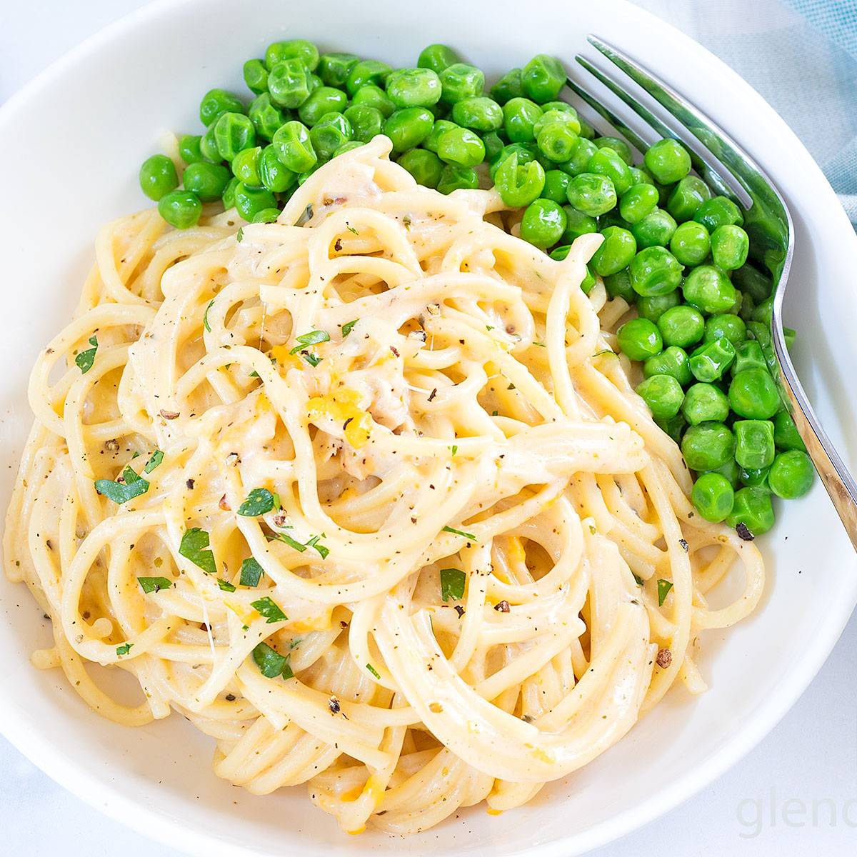 Chicken Tetrazzini in a white ceramic bowl with buttered peas.