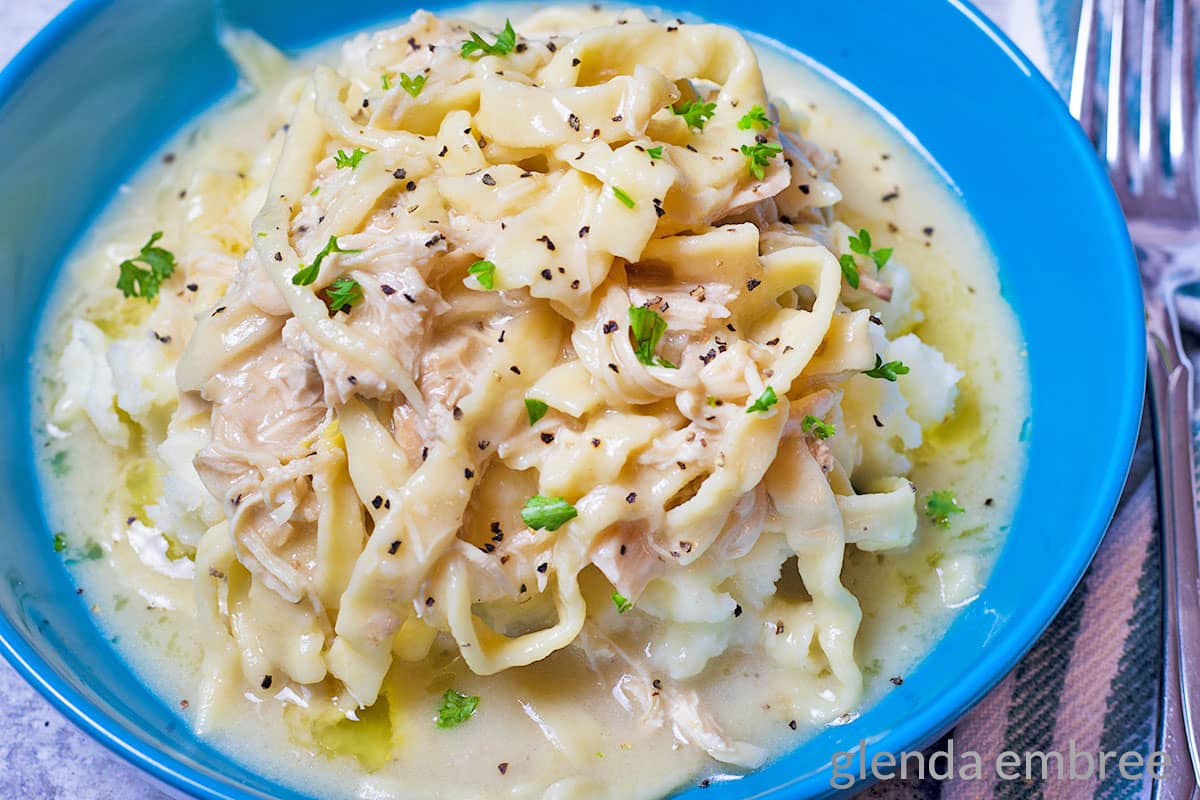 Creamy Chicken and Noodles over mashed potatoes in a blue ceramic bowl.