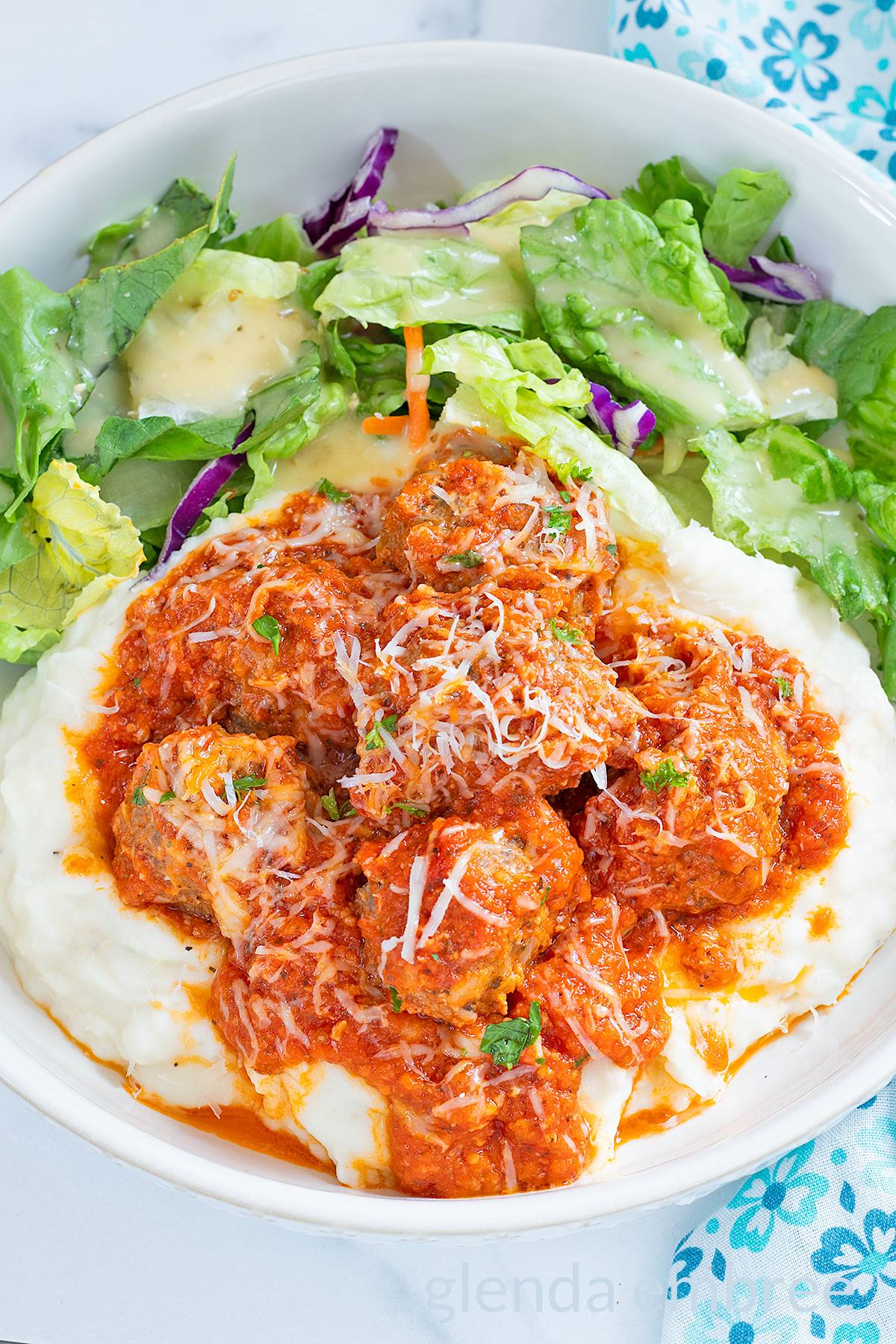 Porcupine meatballs and tomato gravy over mashed potatoes on a white plate with a tossed green salad.