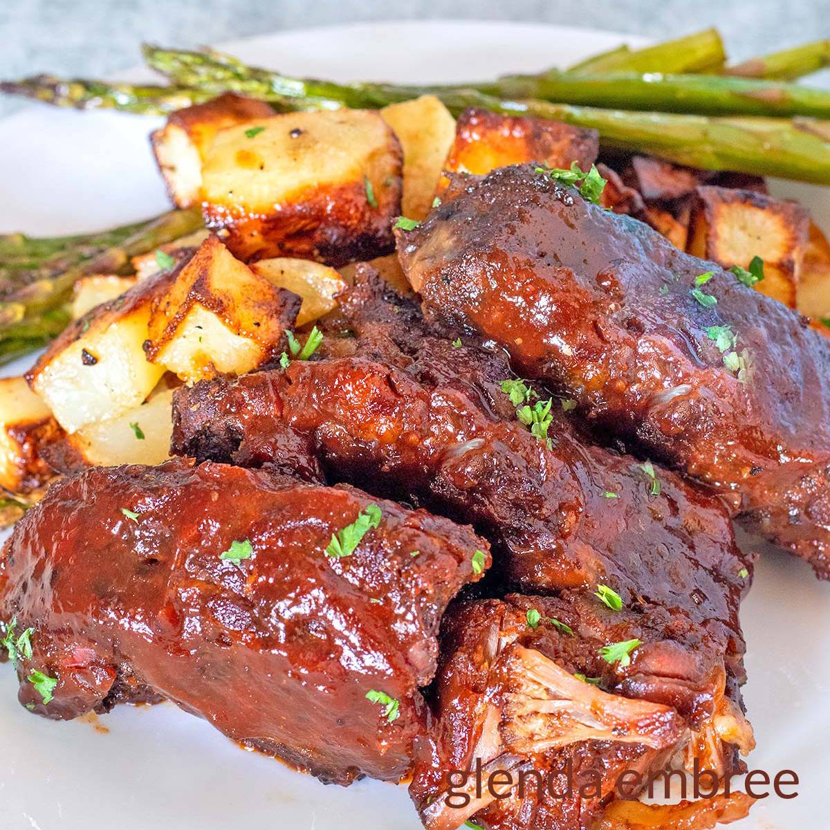 Slow Cooker Country-Style Ribs on a white plate with potatoes and asparagus.