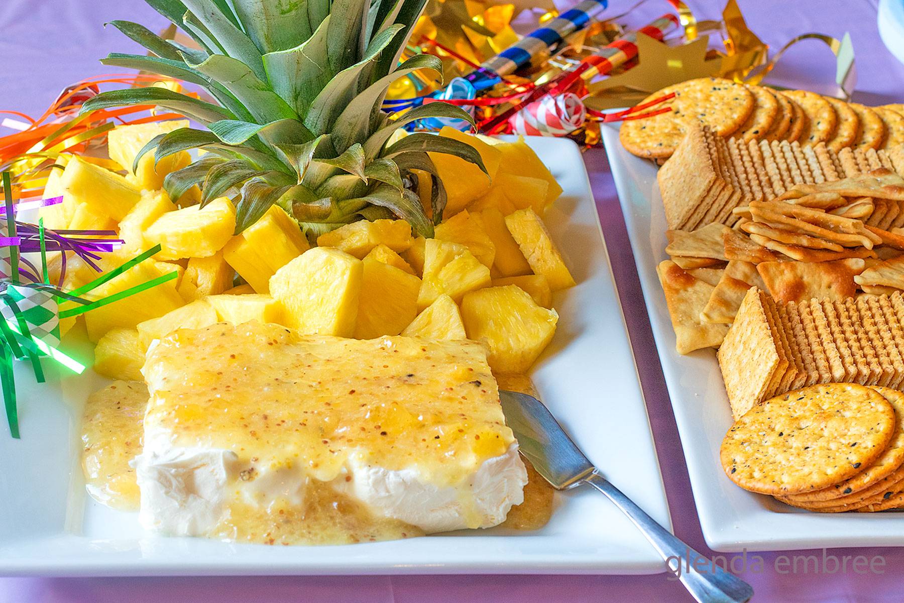 Jezebel Sauce over Cream Cheese on a platter with pineapple chunks next to a second platter with crackers.