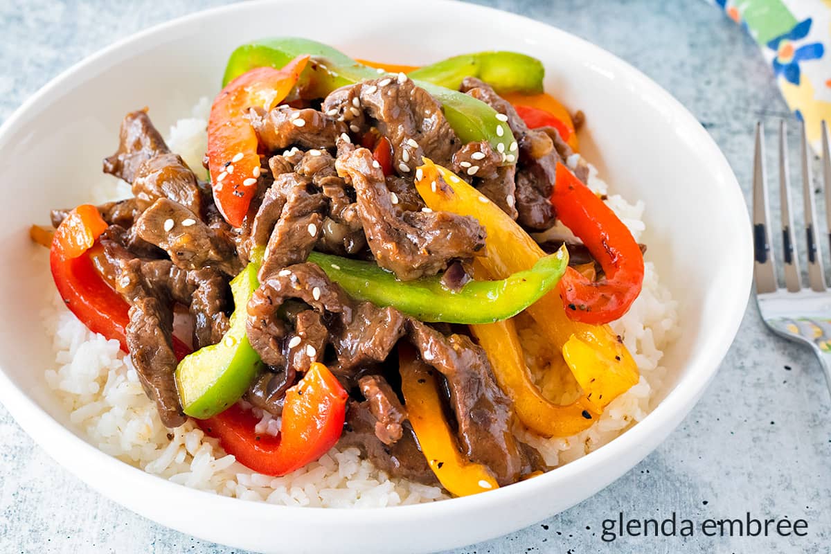 Pepper Steak over rice in a white ceramic bowl.