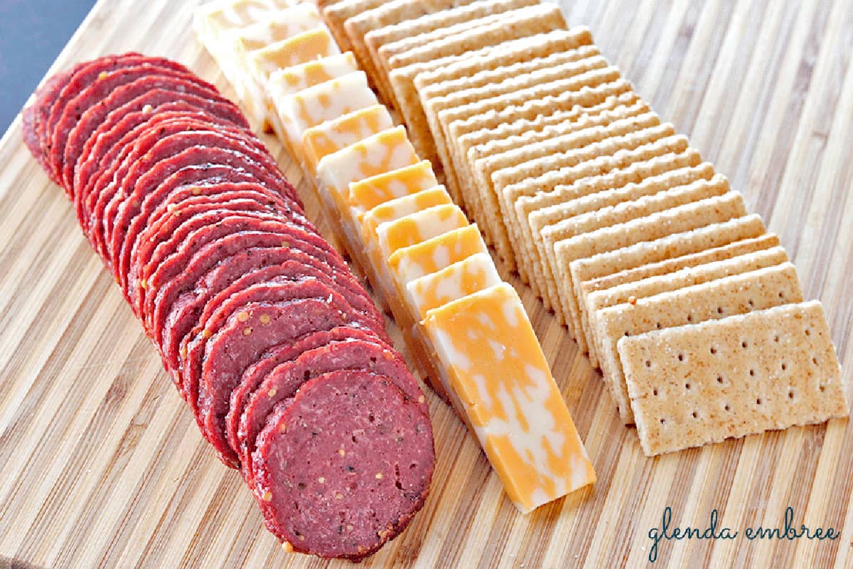 Homemade Beef Summer Sausage on a wooden cutting board with cheese and crackers.