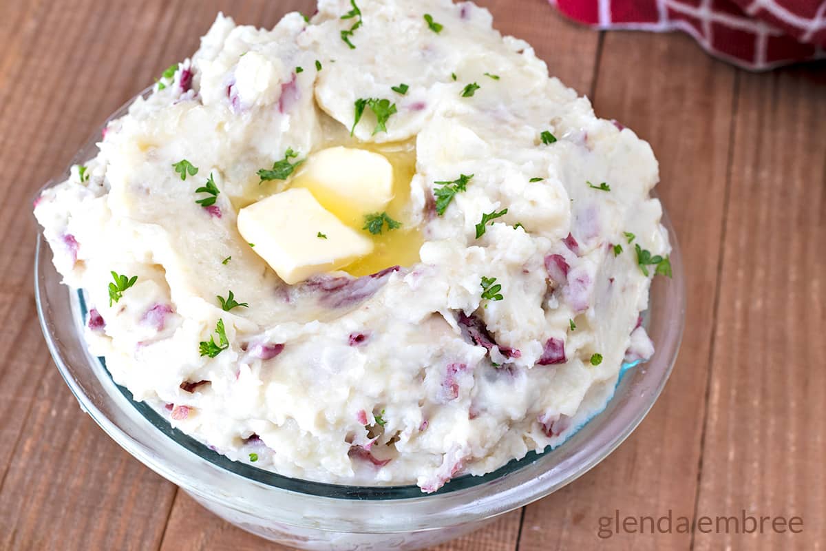 Creamy Red Skin Mashed Potatoes  with melting butter on top in a clear glass serving bowl.