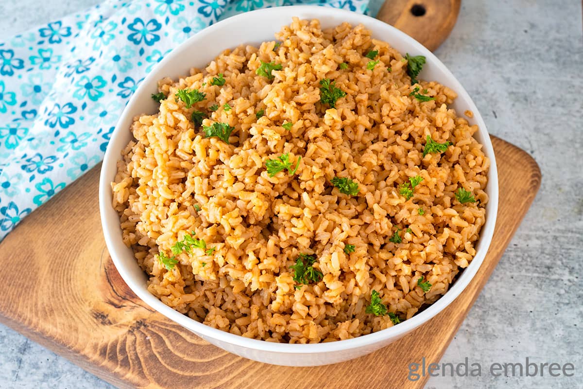 Brown rice in a white serving bowl on a wooden trivet.