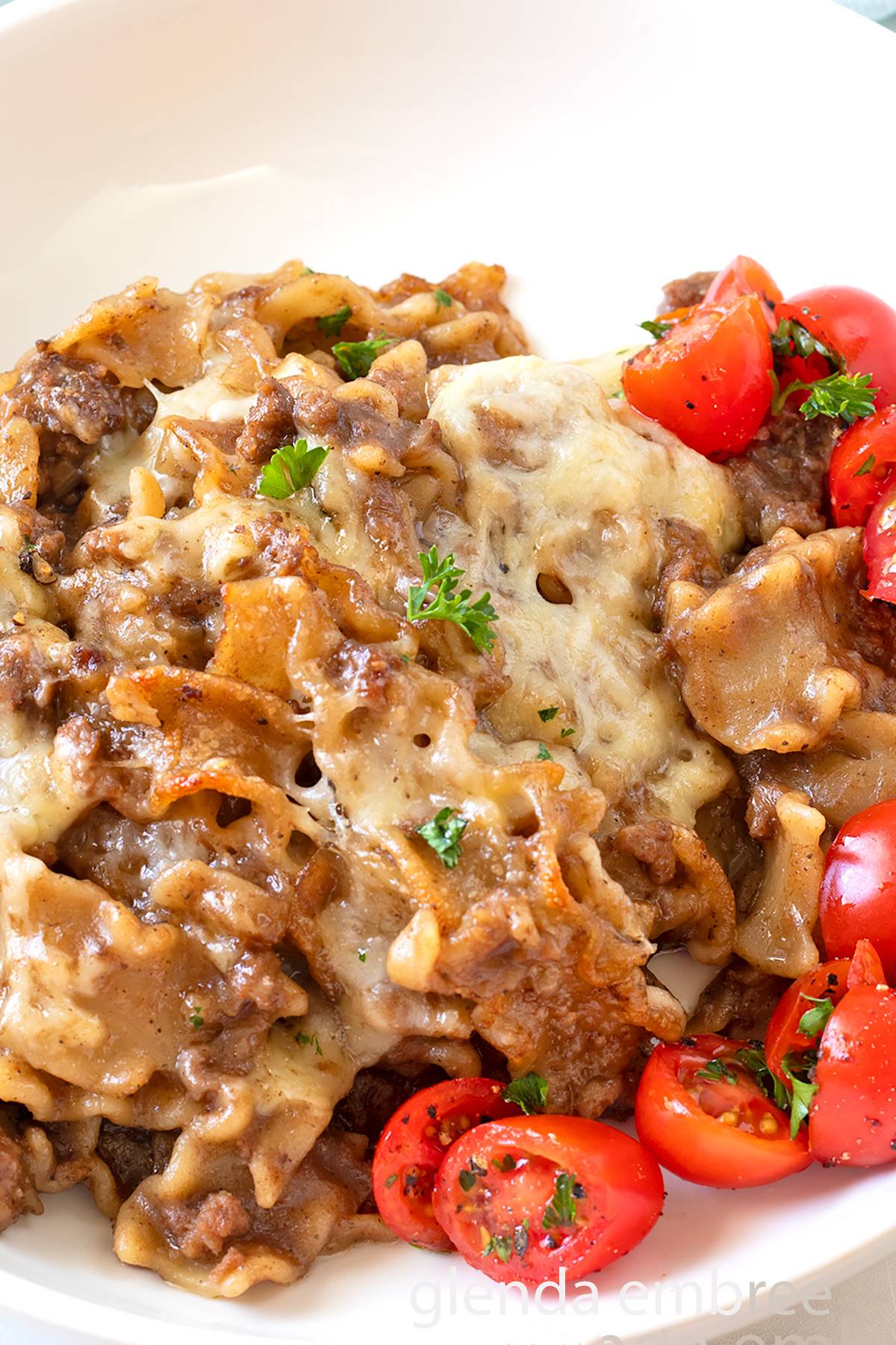 French Onion Beef and Noodles on a white plate with tomato salad.