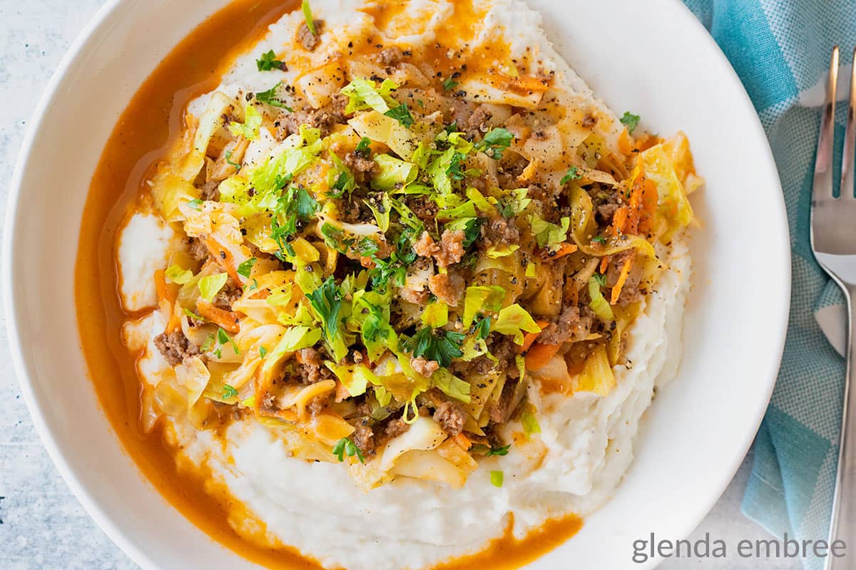 Ground Beef and Cabbage over mashed potatoes in a white bowl.