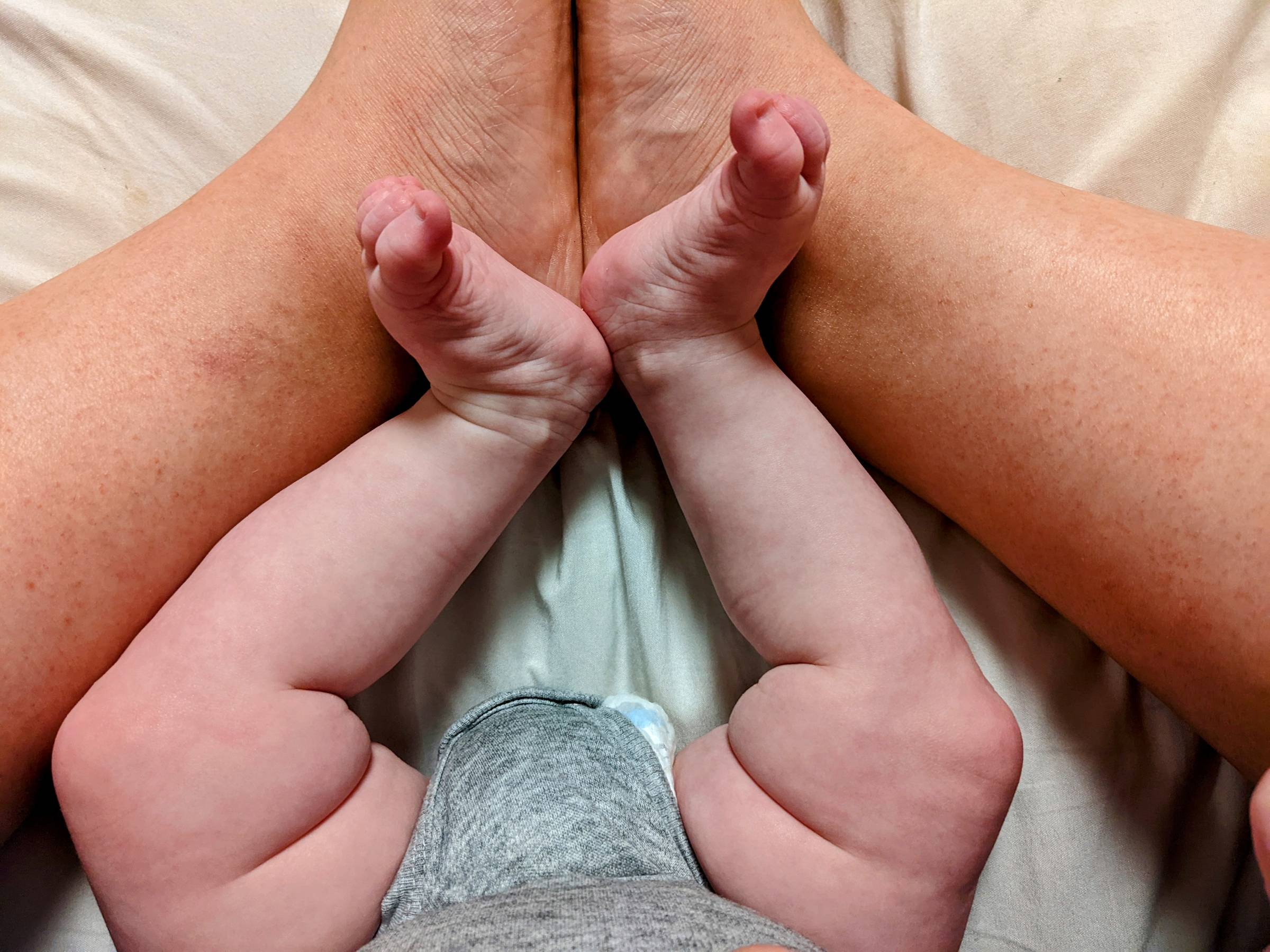 Light pink baby legs nestled inside tan adult legs
