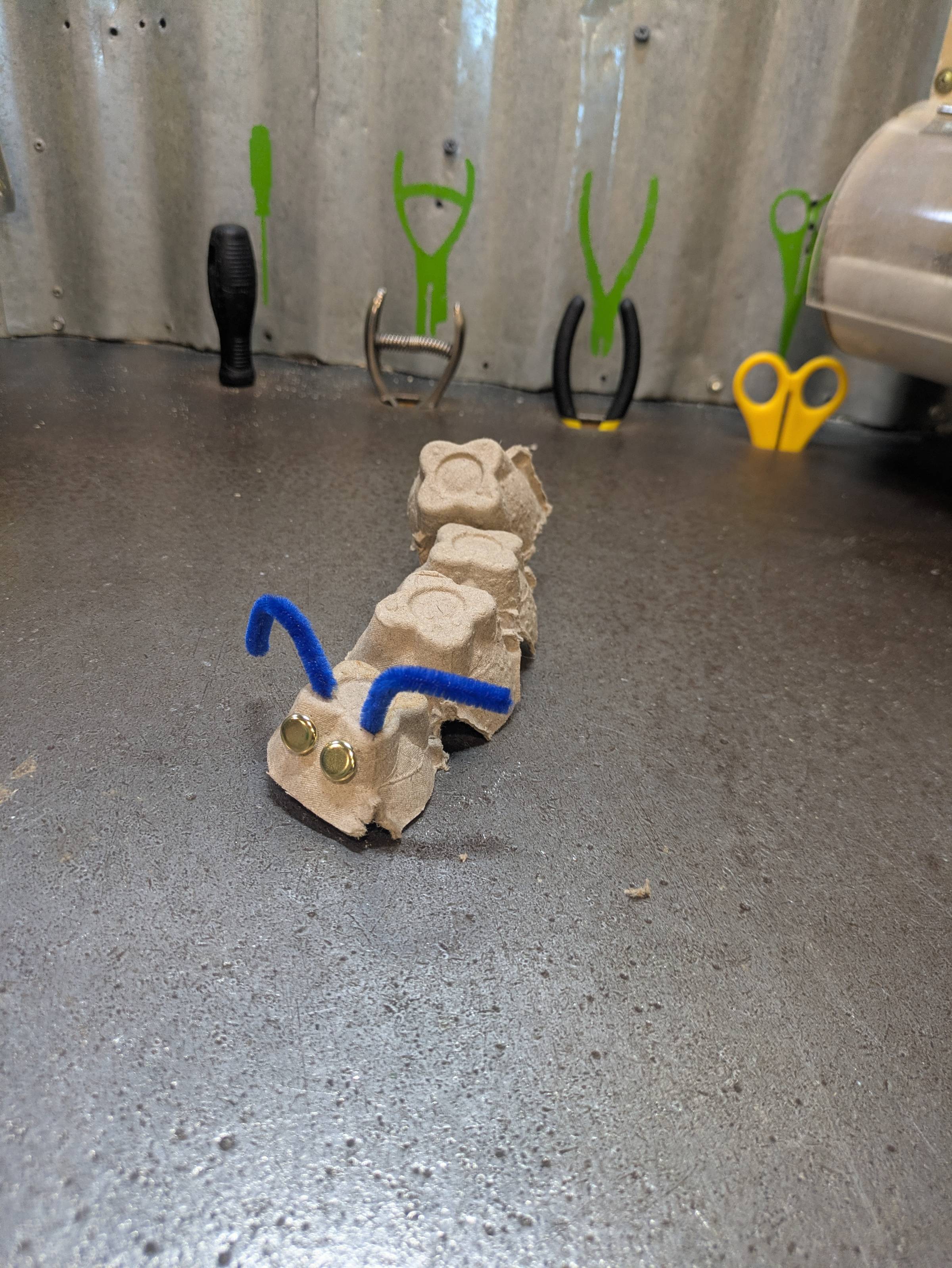 Caterpillar craft made of egg cartons, brads, and pipe cleaners on a workbench