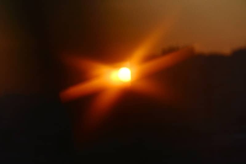 Bright sunburst over dark silhouette of trees