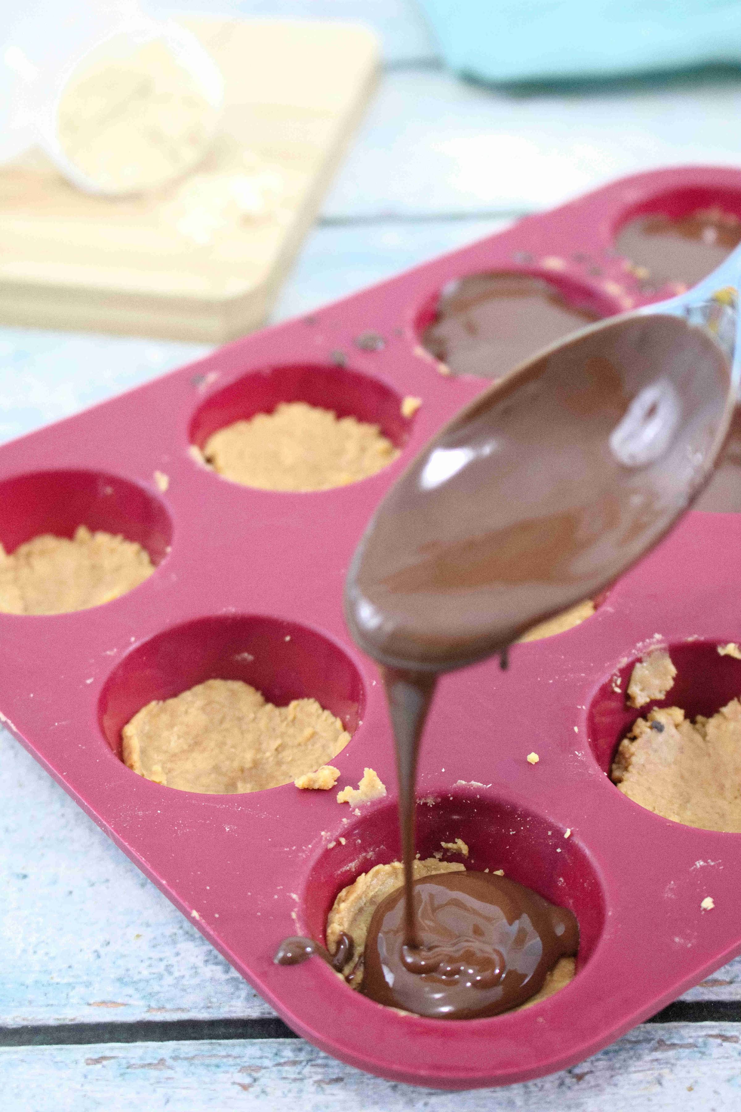 Chocolate being drizzled onto peanut butter protein cups.