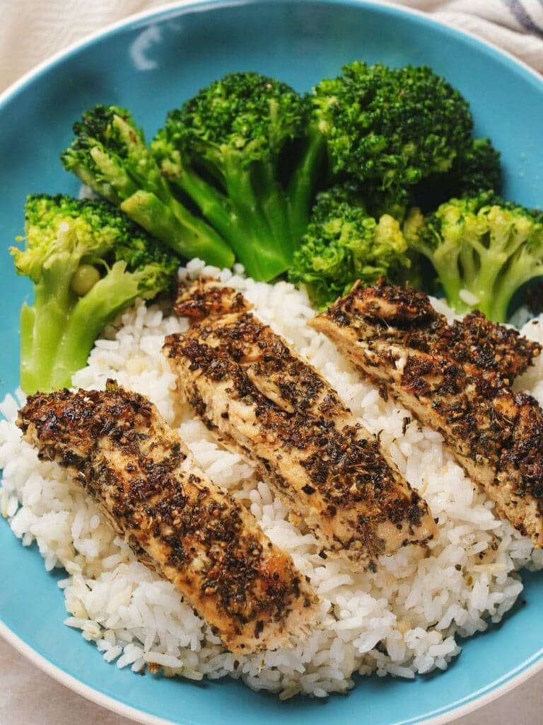 Sliced herbed chicken on rice with broccoli.