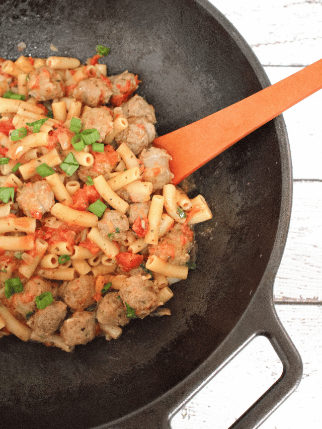Sausage pasta with tomatoes and green onions in a cast iron pot.