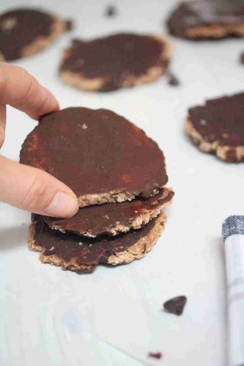 Three cookies topped in chocolate and being stacked.