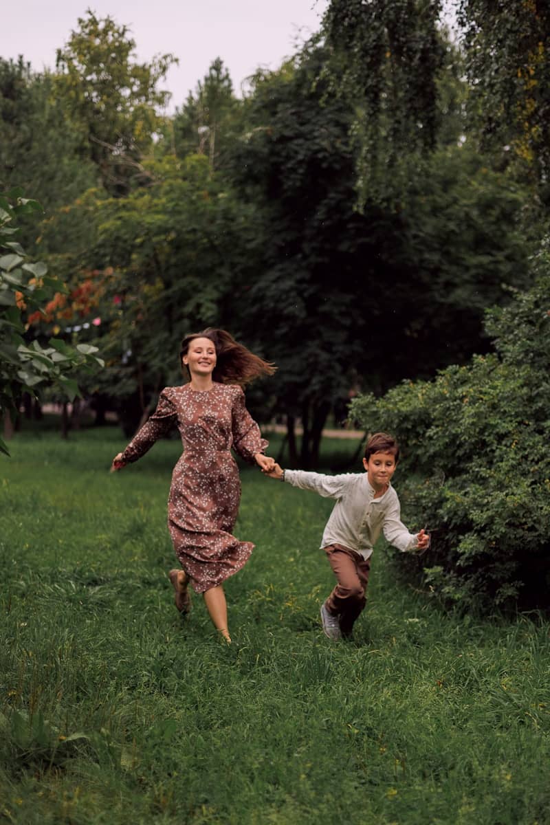 A woman and a boy running through a grassy park.