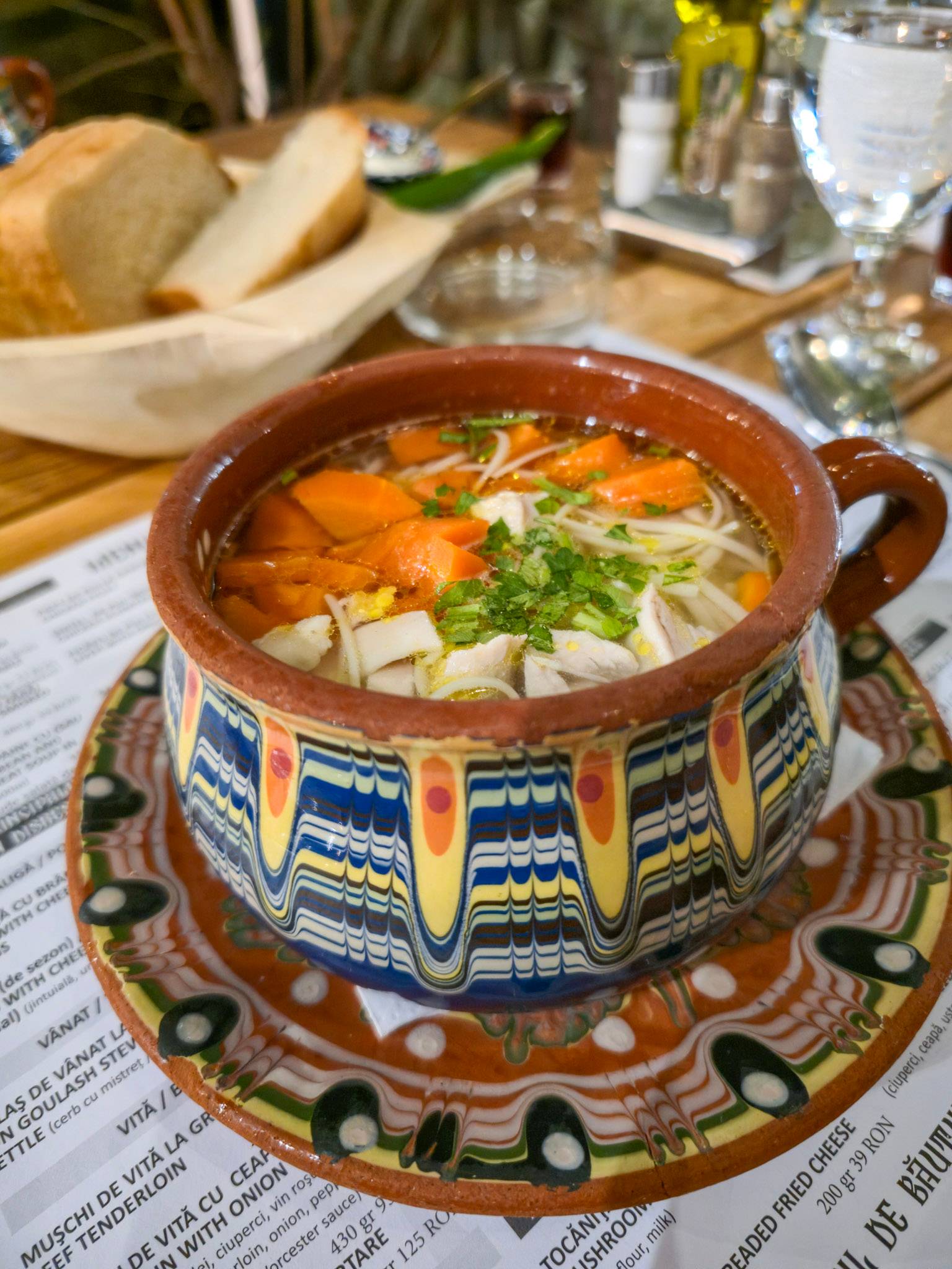 A traditional Romanian chicken and noodle soup served in  a painted clay bowl.