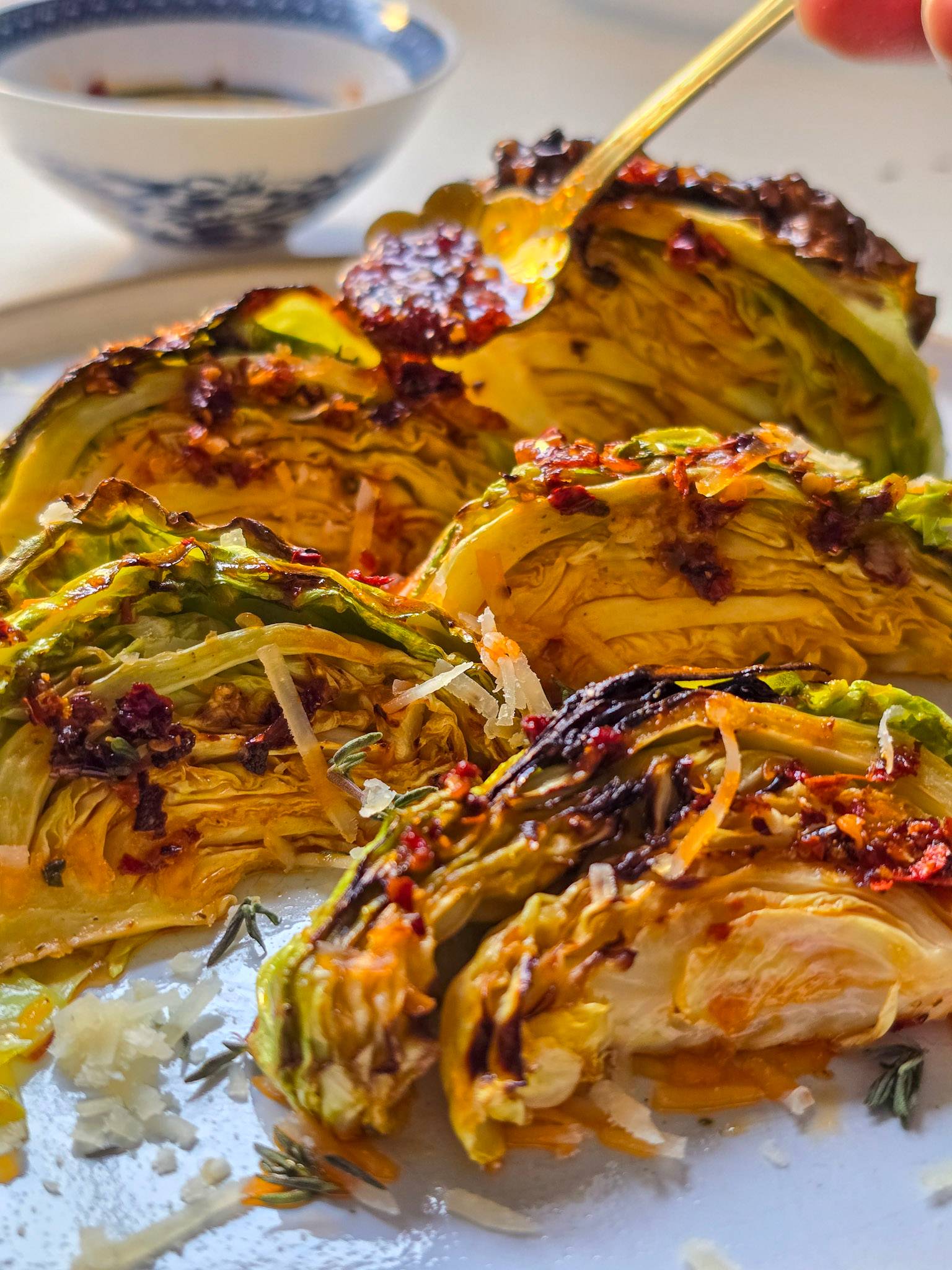 Air fryer cabbage wedges served on a grey plate with chili oil drizzles, scattered herbs, and grated Parmesan on top.