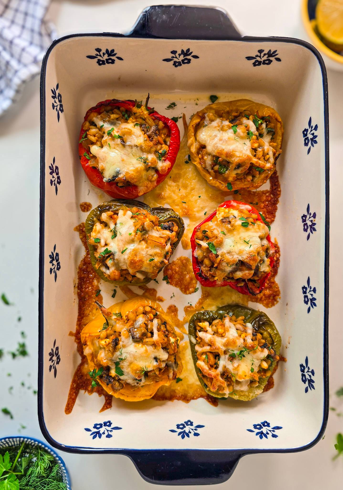 Barley stuffed peppers with melted cheese and fresh herbs on top in blue and white baking dish.
