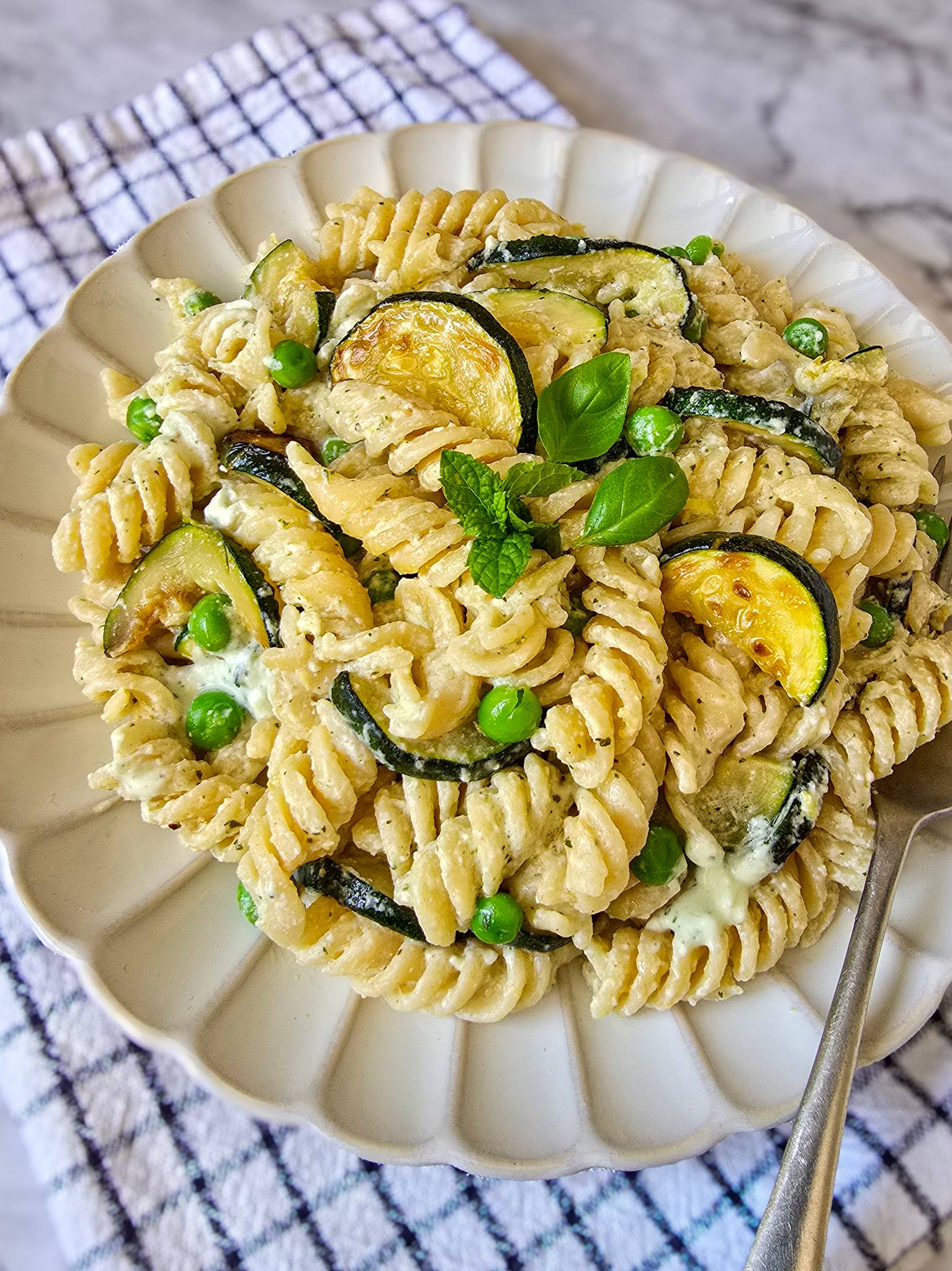Zucchini fusilli pasta with whipped feta sauce, peas, basil and mint on top.
