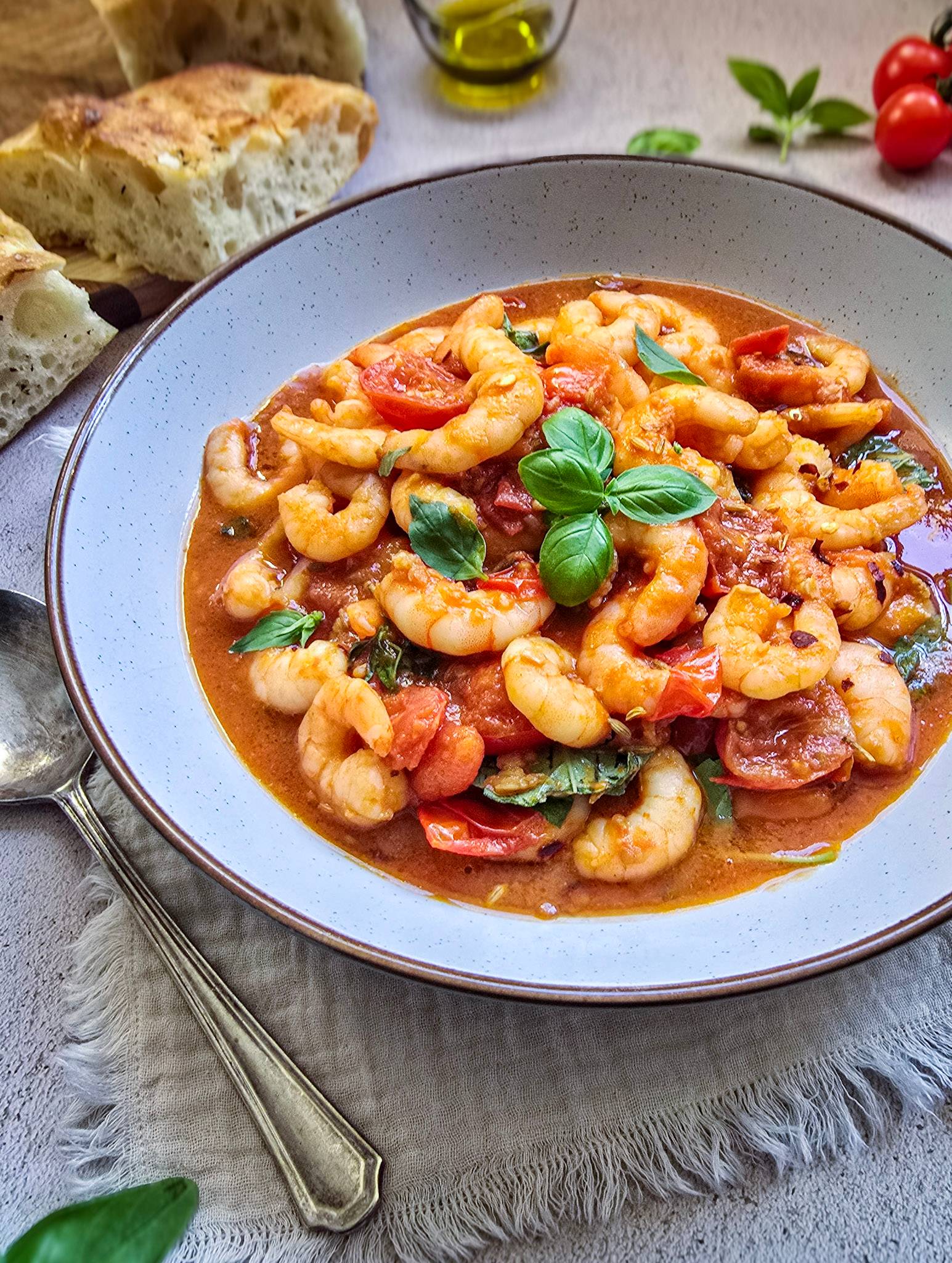 a bowl of shrimp marinara with cherry tomatoes and basil.