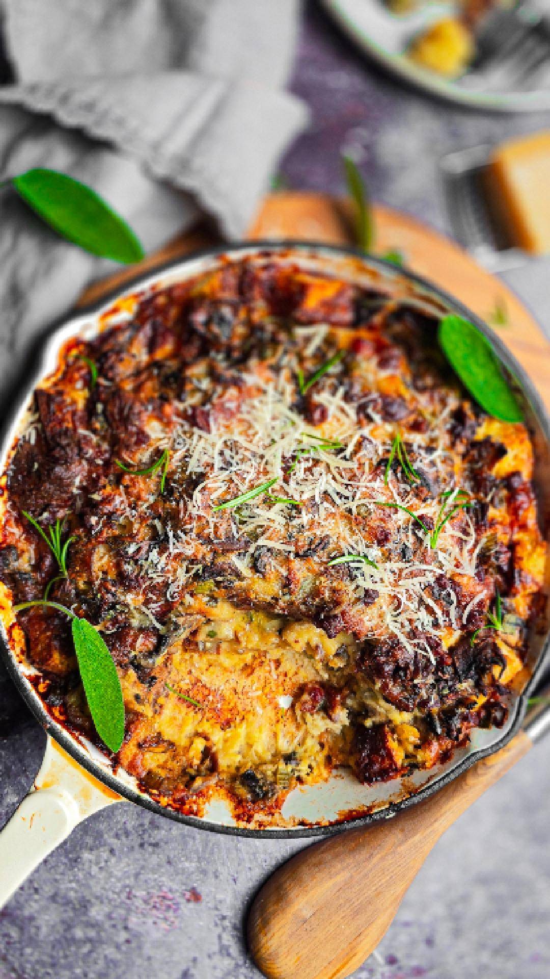 Golden baked breakfast strata, a savoury bread and butter pudding with pancetta, mushrooms and herbs in a cream enamel pan, slice scooped out.