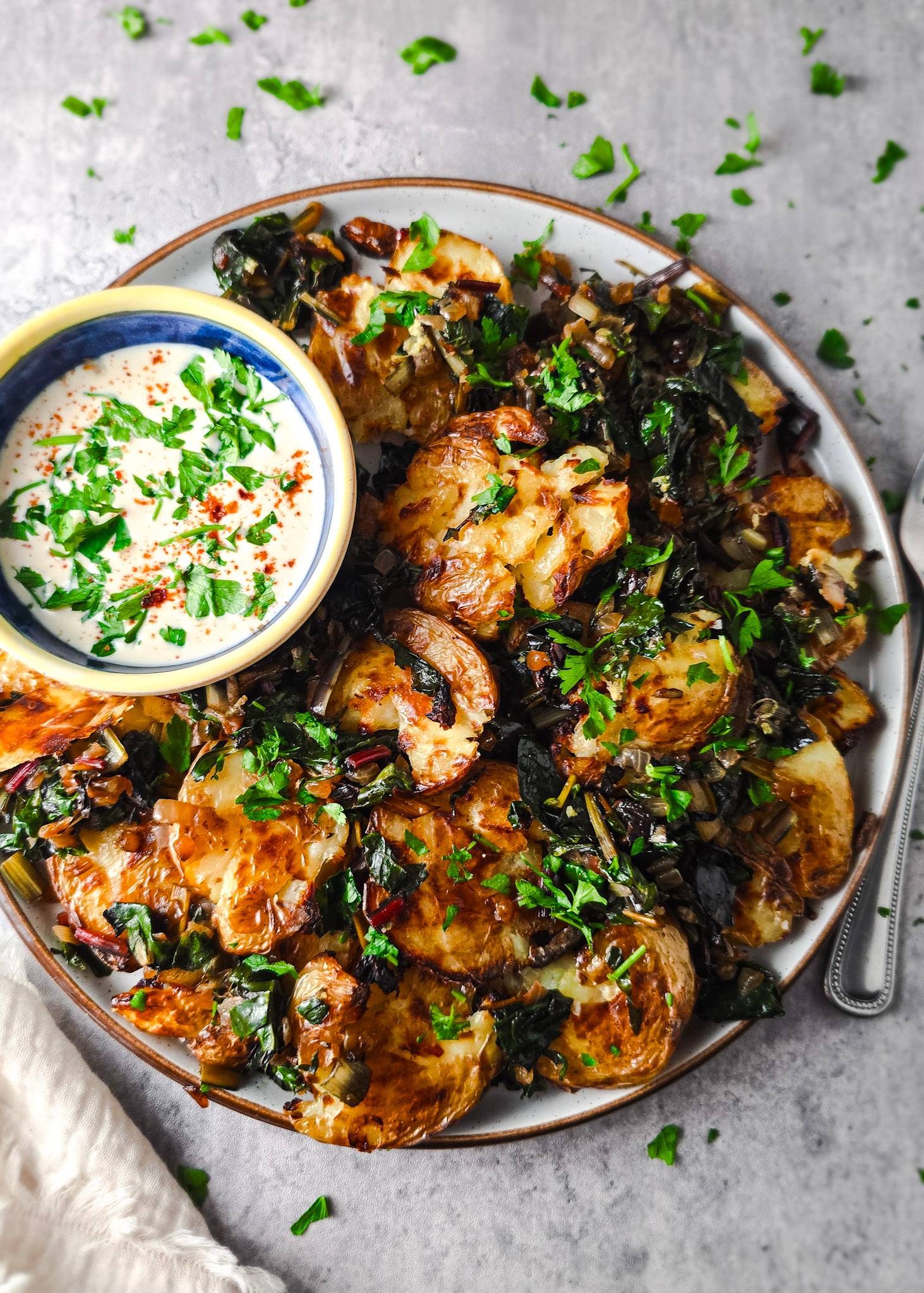 A plate full of crispy potatoes, sauteed swiss chard and a creamy dressing with chopped parsley.