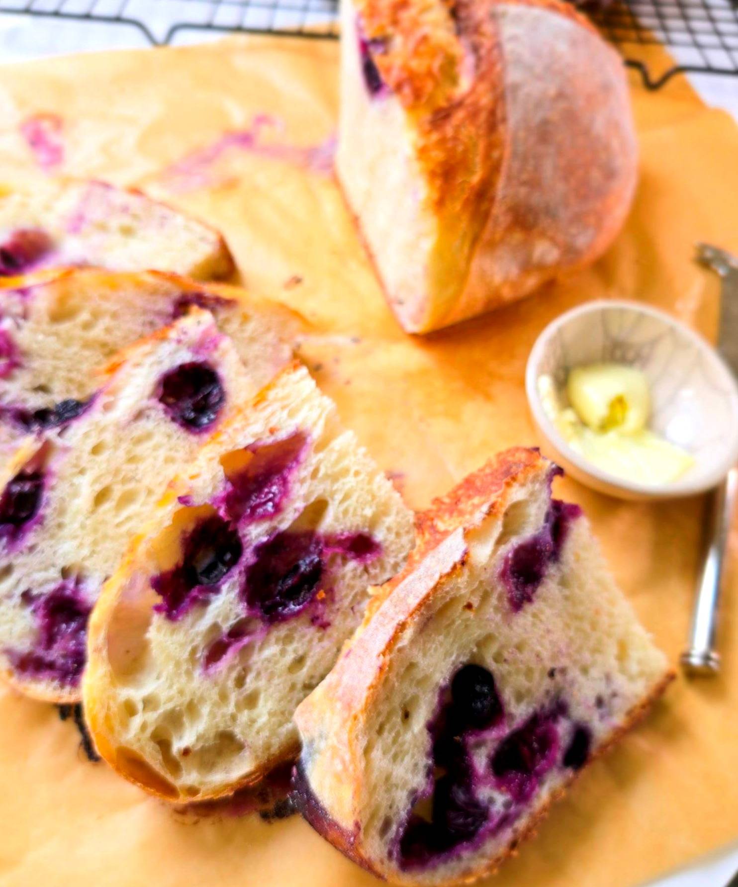 Sliced blueberry sourdough with tangzhong on parchment paper with a small butter dish next to it.