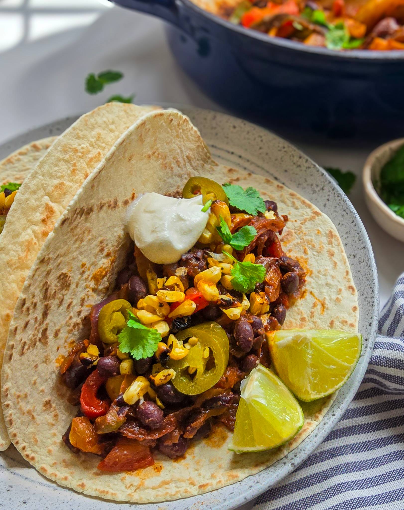 A loaded fajita with black beans, sour cream, jalapenos. corn and lime wedges.