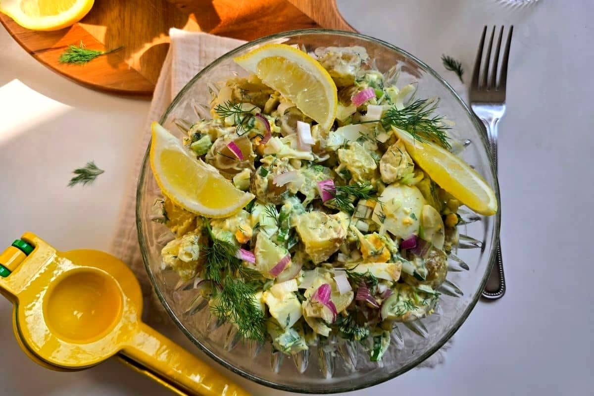 A potato salad with spring onion, dill, red onions and lemon wedges.