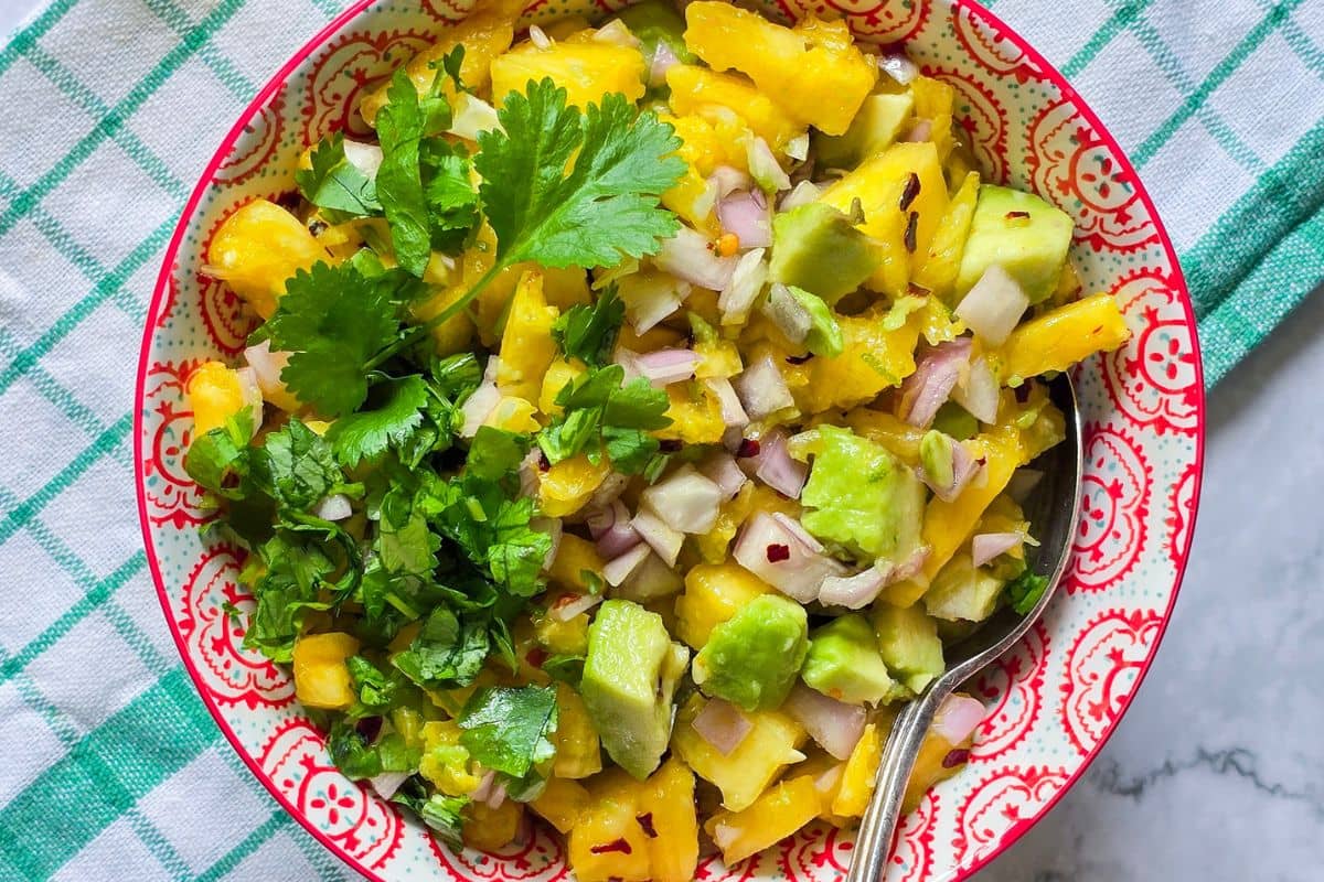 A fesh pineapple and avocado salsa with lots of cilantro and shallots in a patterned red bowl. 