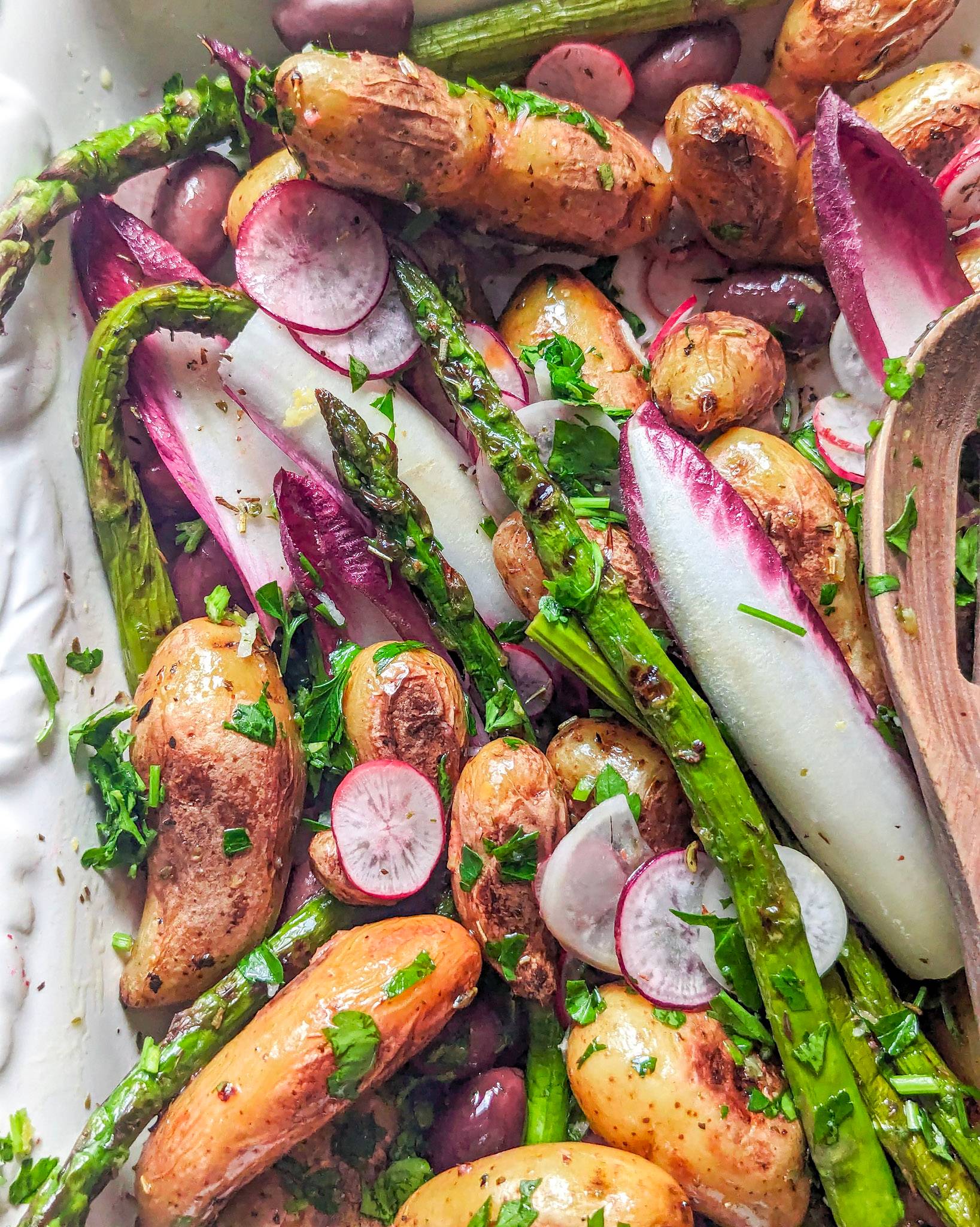 A potato asparagus salad on a white platter with plenty of herbs radishes and chicory.