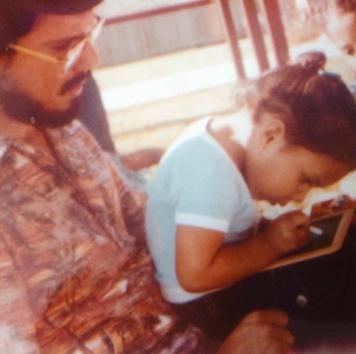 vintage 1970s photo of little Brandi intensely writing on a chalkboard on her dad's lap,